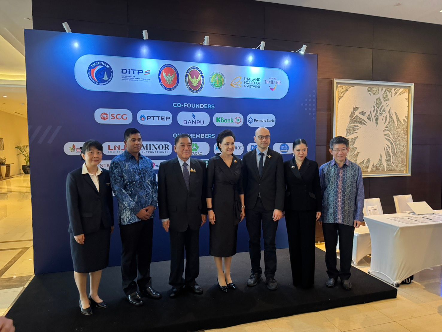 A group of seven people, four men and three women, stand formally at an event.