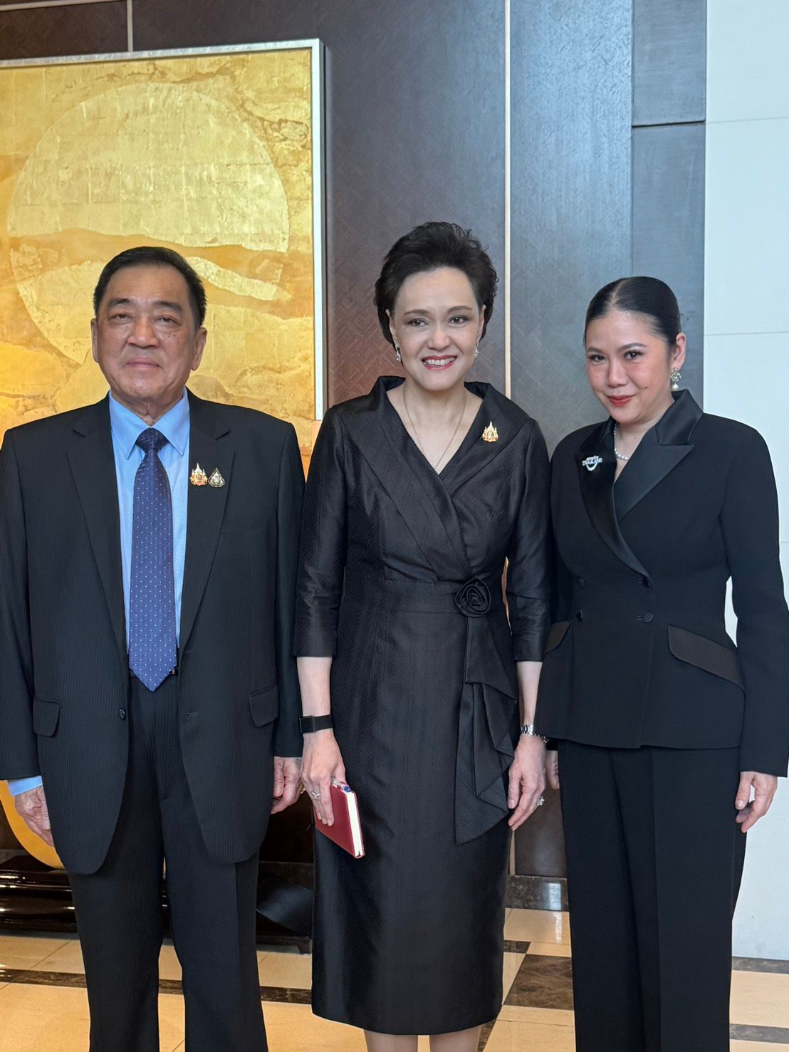 Three formally dressed individuals, a man and two women, pose together in an elegant indoor setting.