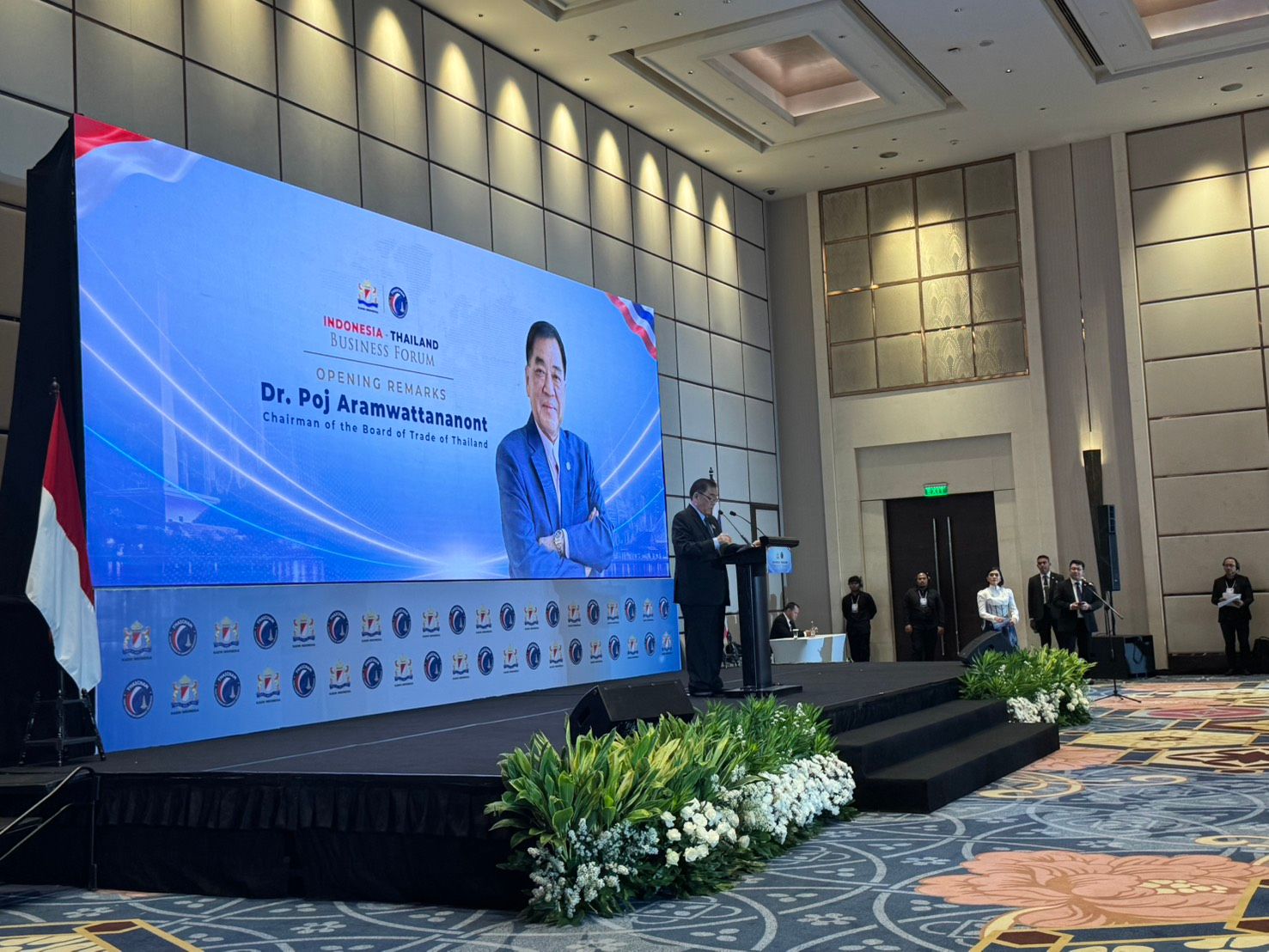 Speaker presents on stage, large screen shows Dr. Pug Anantanasuwong and presentation graphics.
