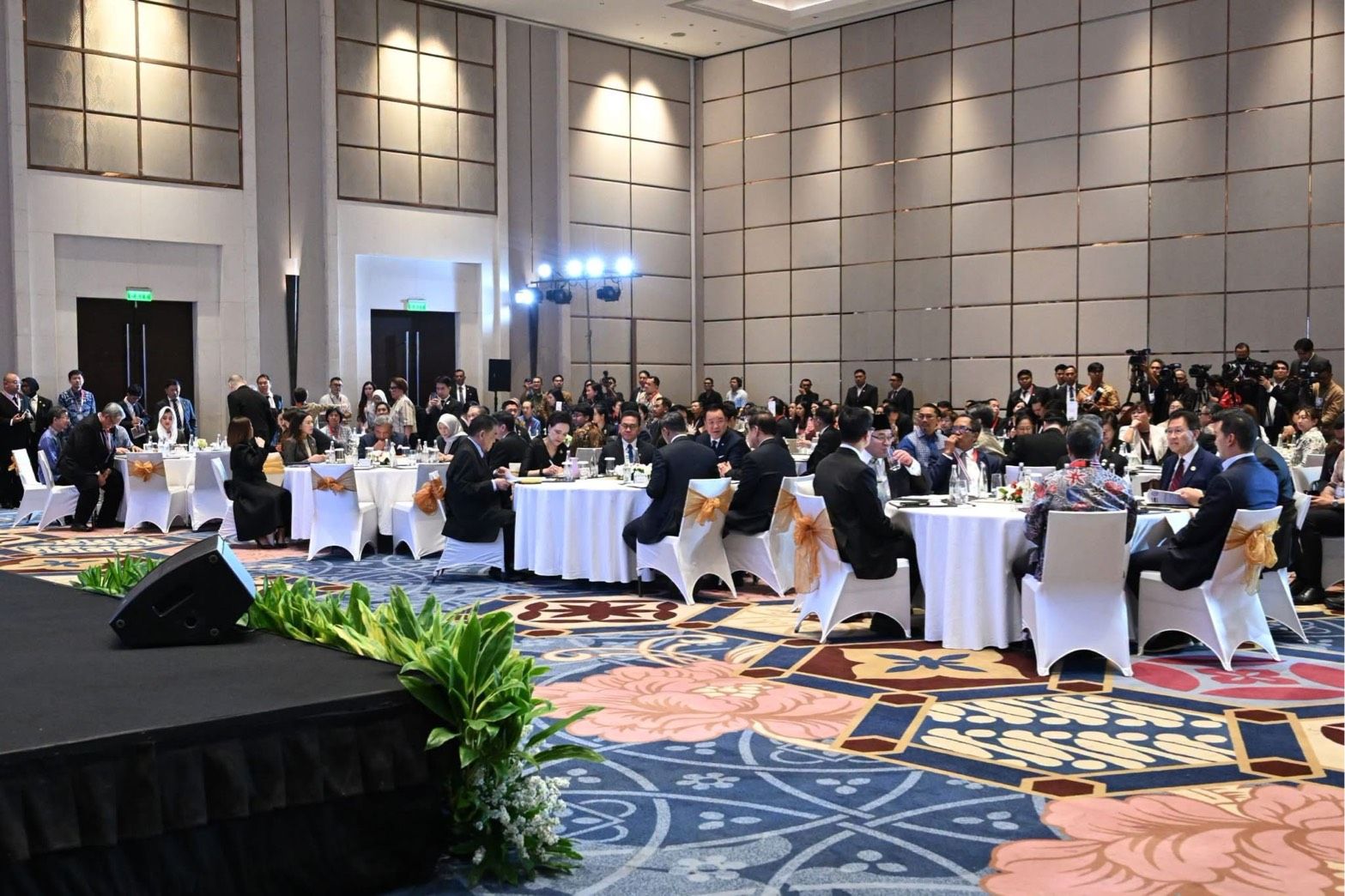 Attendees seated at round tables in a large, elegant conference hall for an event.