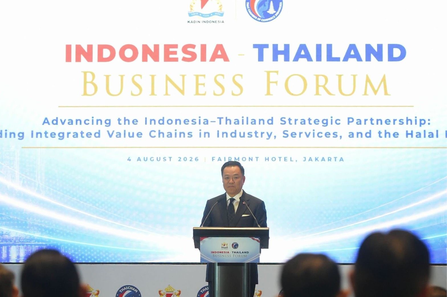 Man speaks at podium before 'Indonesia Thailand Business Forum' banner, addressing attendees.