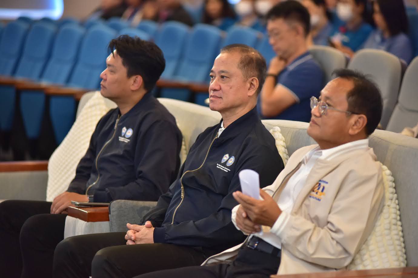 Three men seated in an audience, attentively observing a presentation or event.