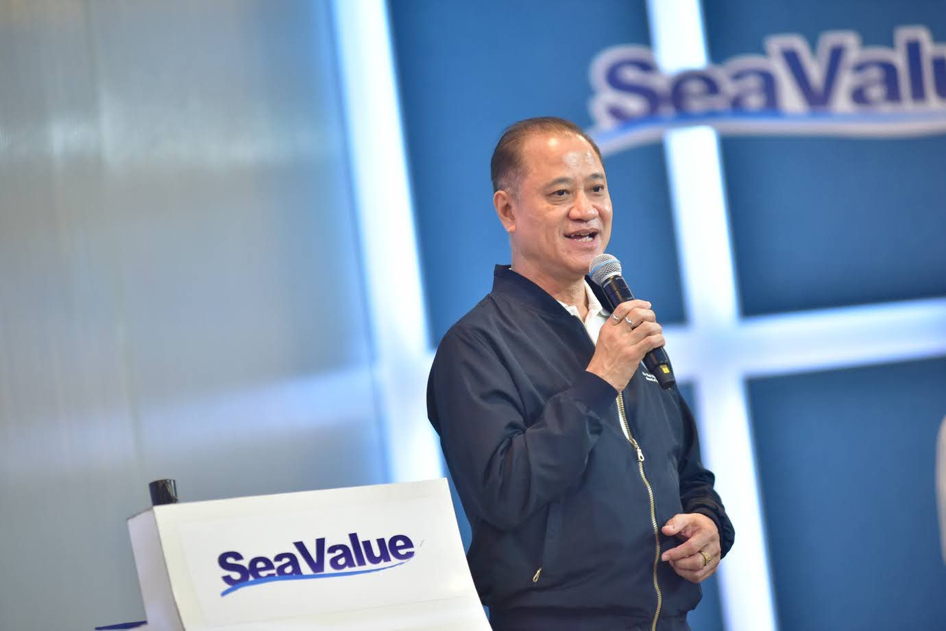A smiling man in a dark jacket speaks into a microphone at a SeaValue event.
