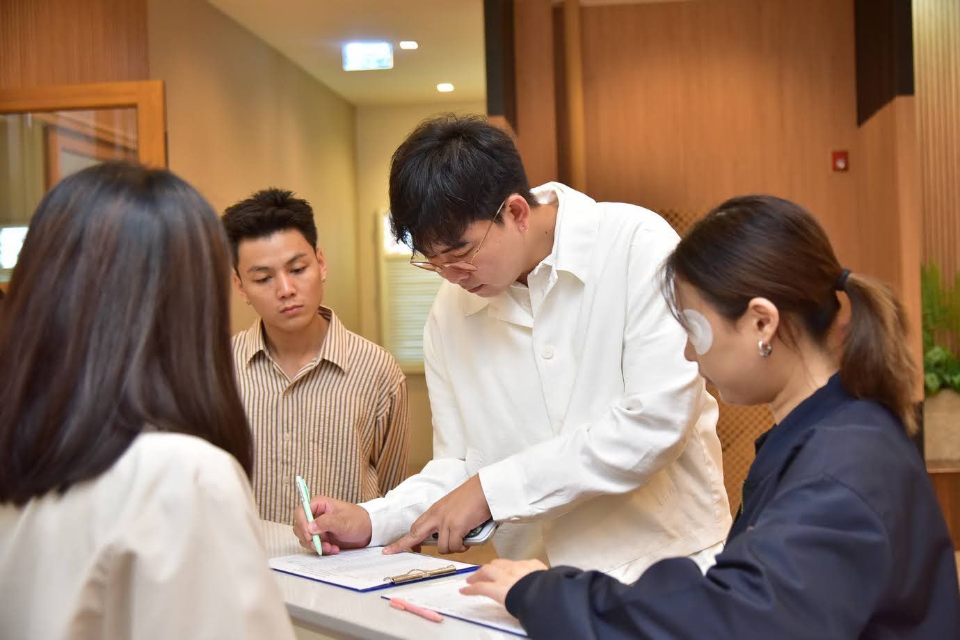 Man in white shirt points at documents while a woman writes, observed by two others.