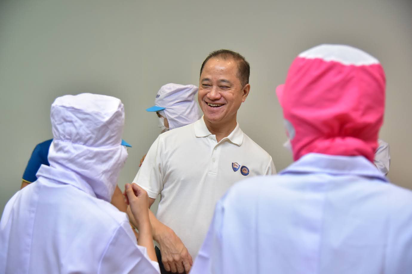 Smiling man in polo shirt conversing with workers wearing protective gear in a facility.