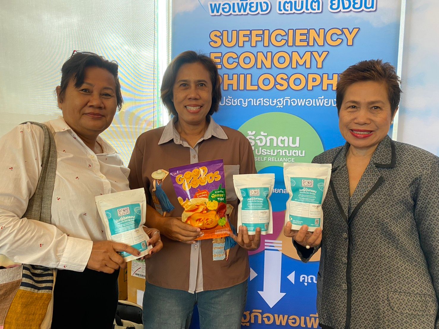 Three women smiling, holding various packaged products in front of a philosophy banner.