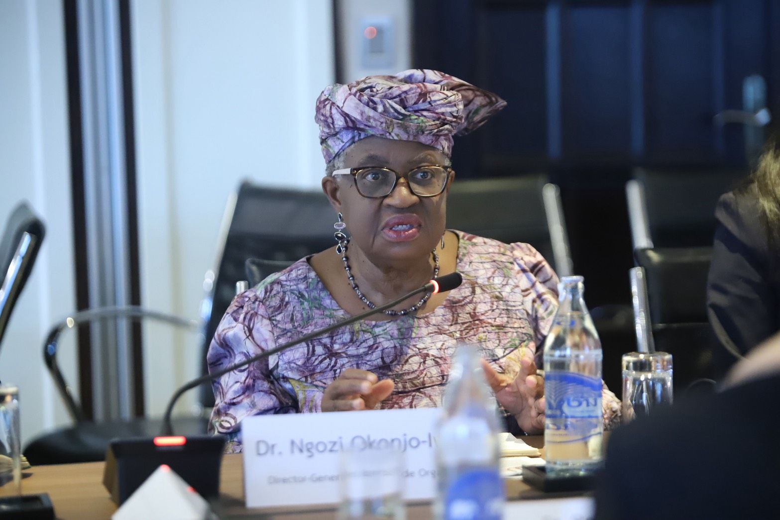 Dr. Ngozi Okonjo-Iweala speaks at a conference, wearing a purple patterned outfit and glasses.