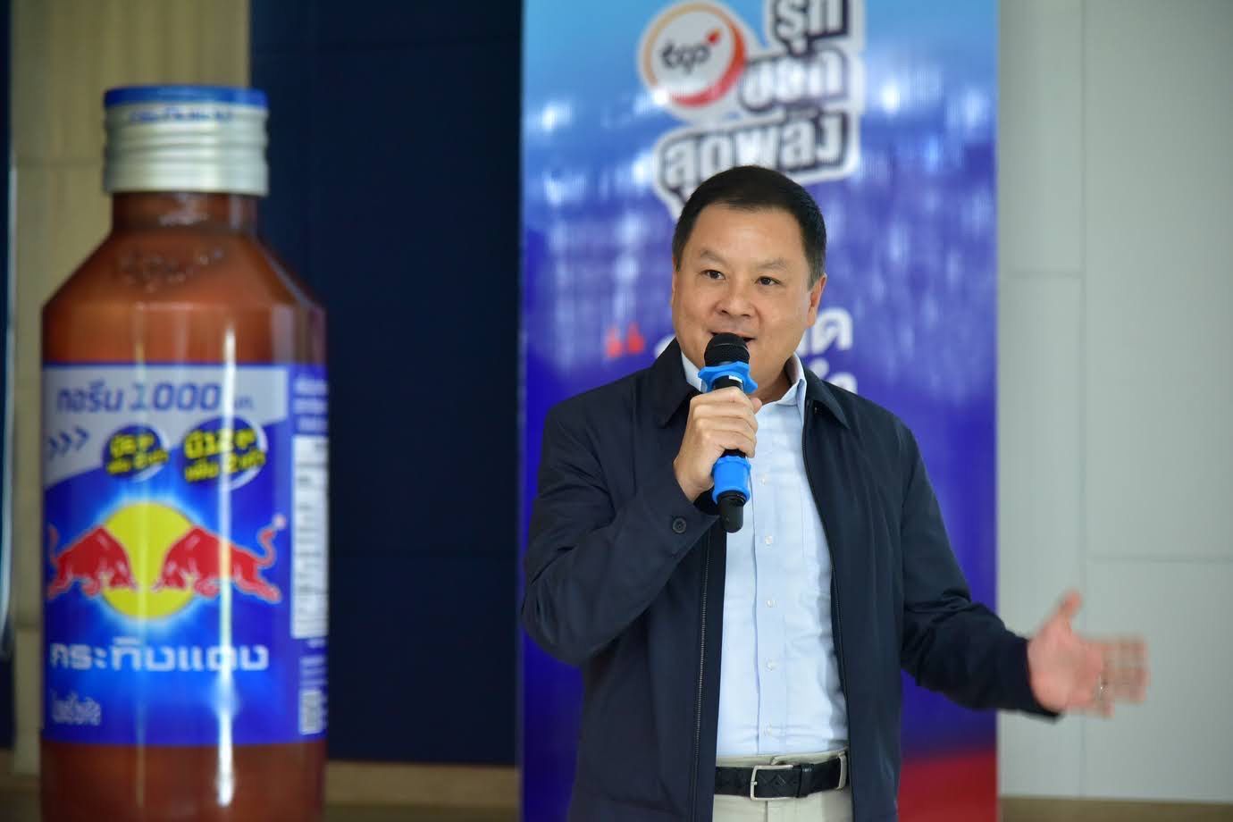 Man in blue jacket speaks next to a giant bottle of Krating Daeng Red Bull.