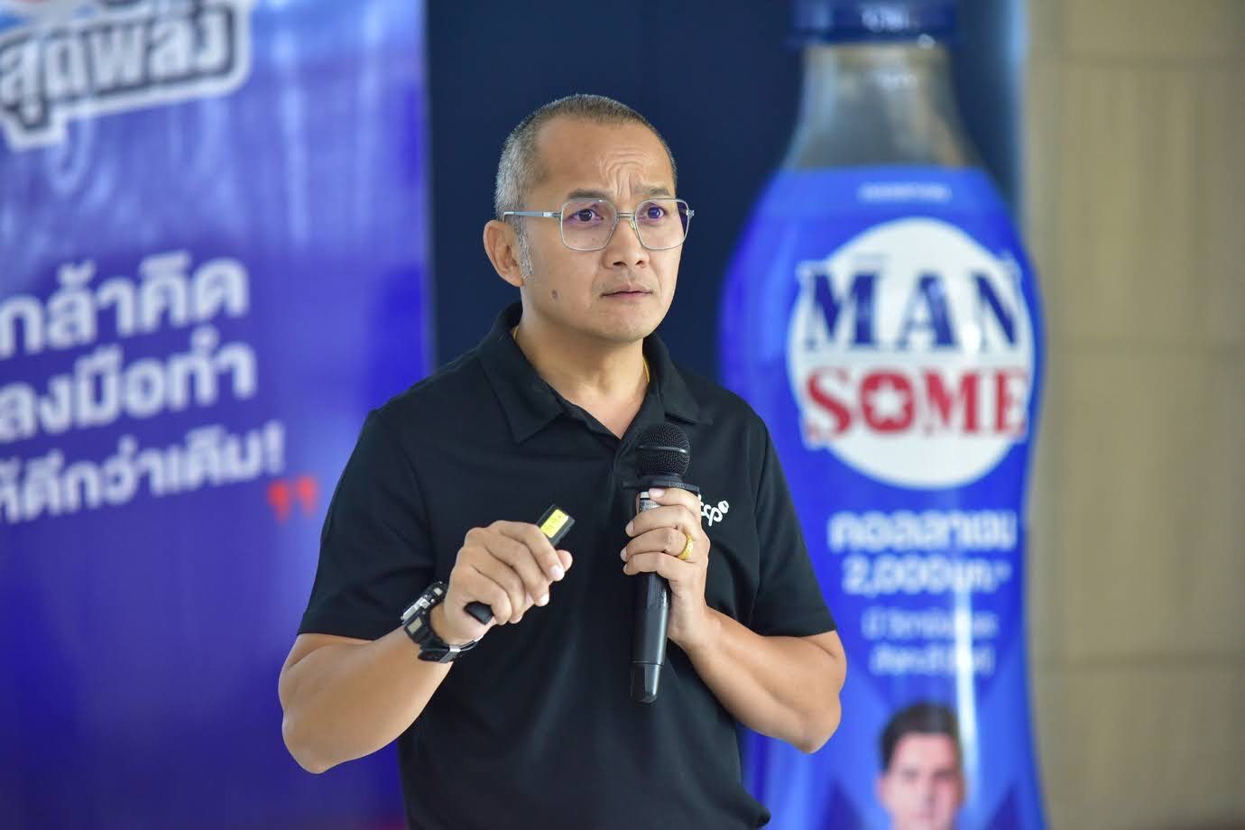 Man in glasses speaking into a microphone with a yellow pointer, in front of a “MAN SOME” banner.