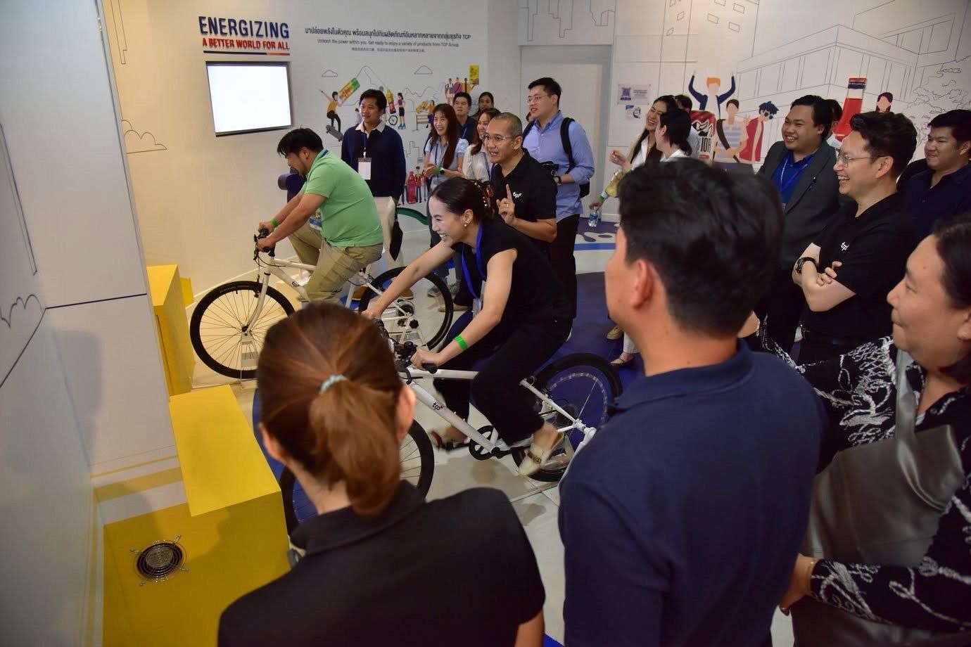 Attendees participate in an interactive exhibit, pedaling stationary bikes while others observe.