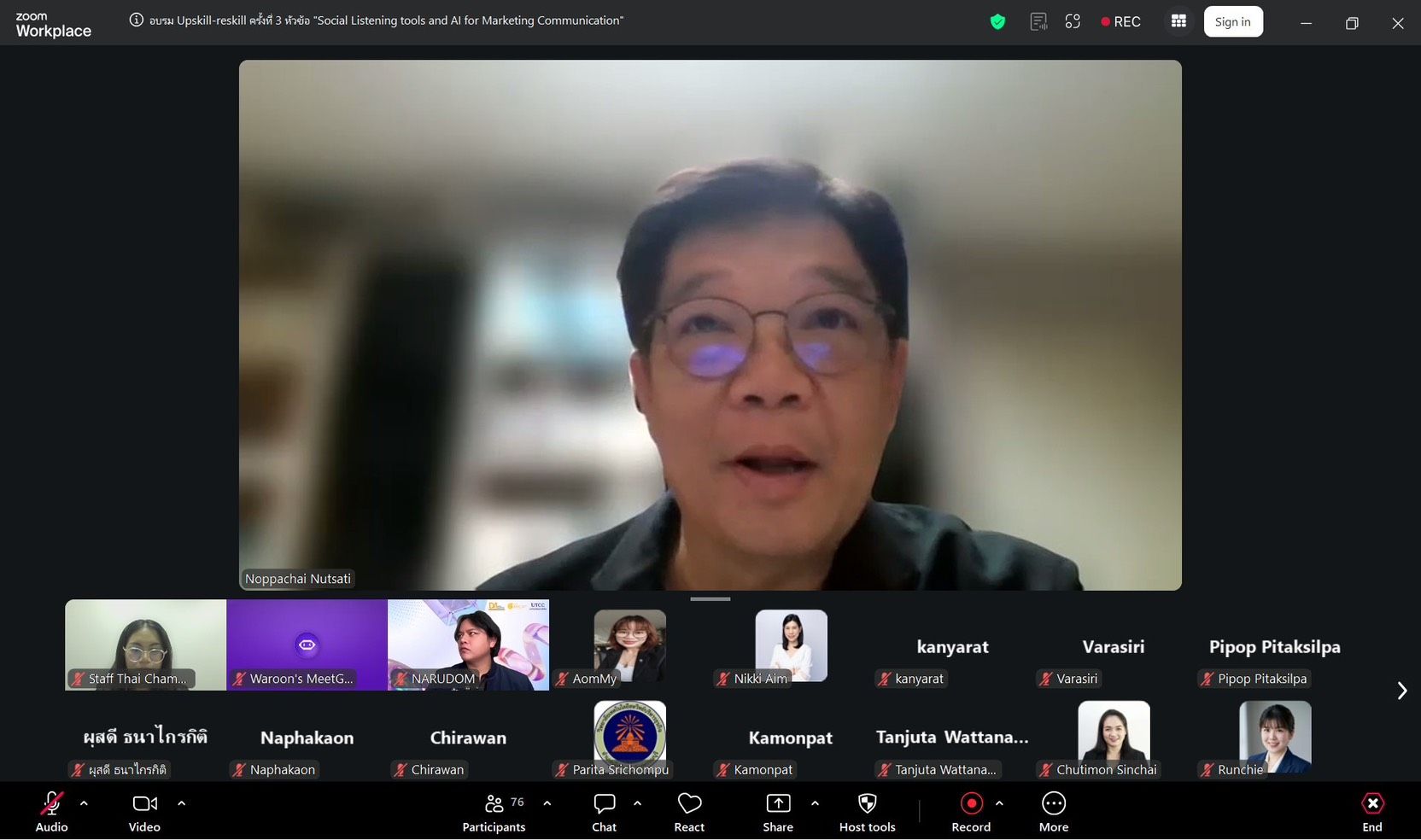 Man with glasses speaking during a video conference, with multiple participants visible below.