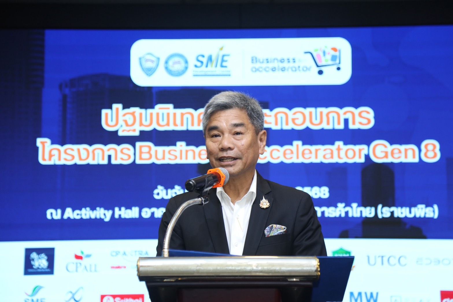 Man in a suit speaks at a podium during the Business Accelerator Gen 8 event.