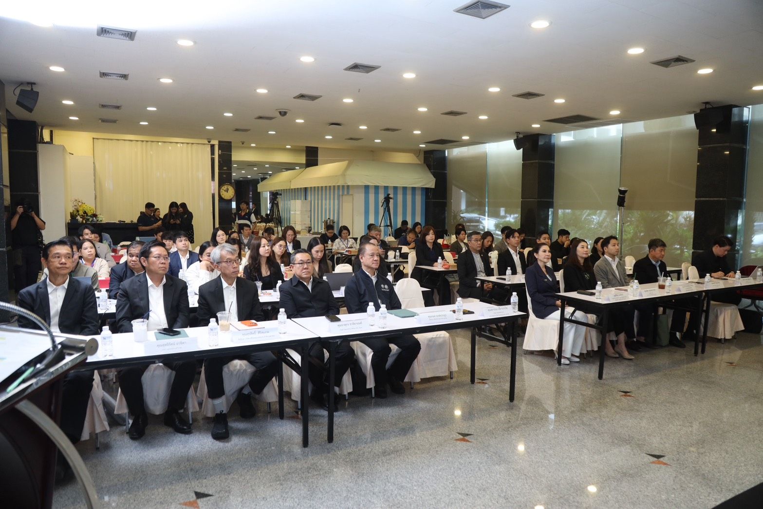 Conference attendees seated at long tables in a brightly lit event hall.