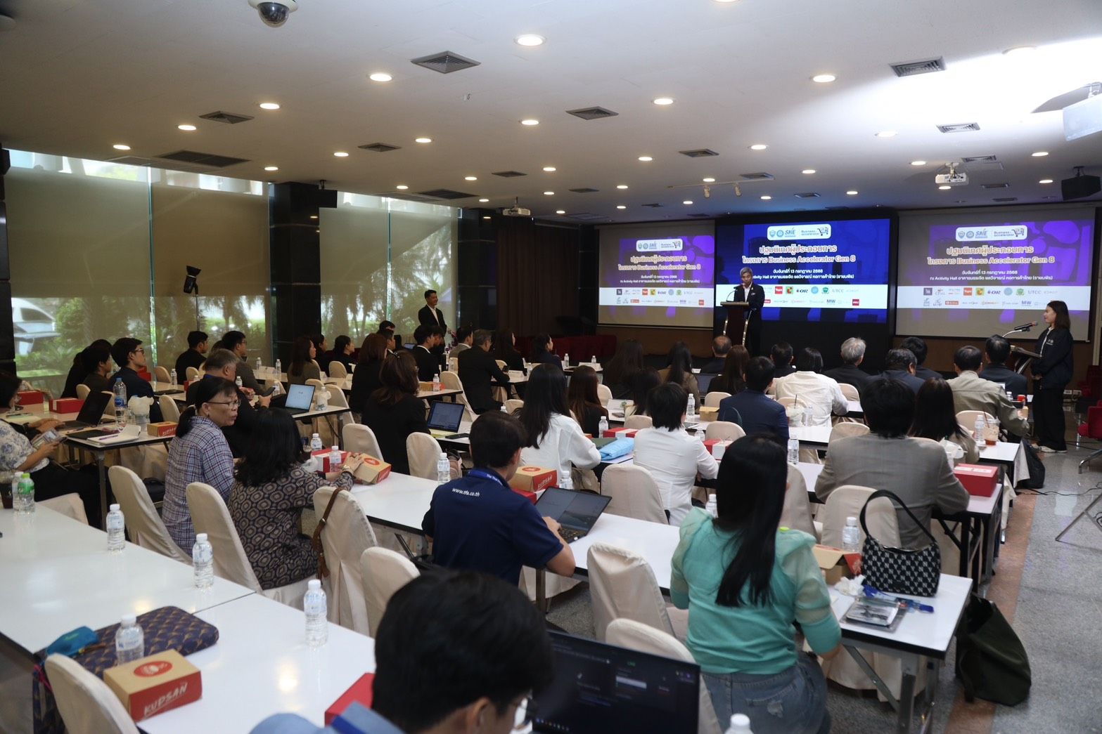 Large conference room with many attendees watching presentations on multiple screens.