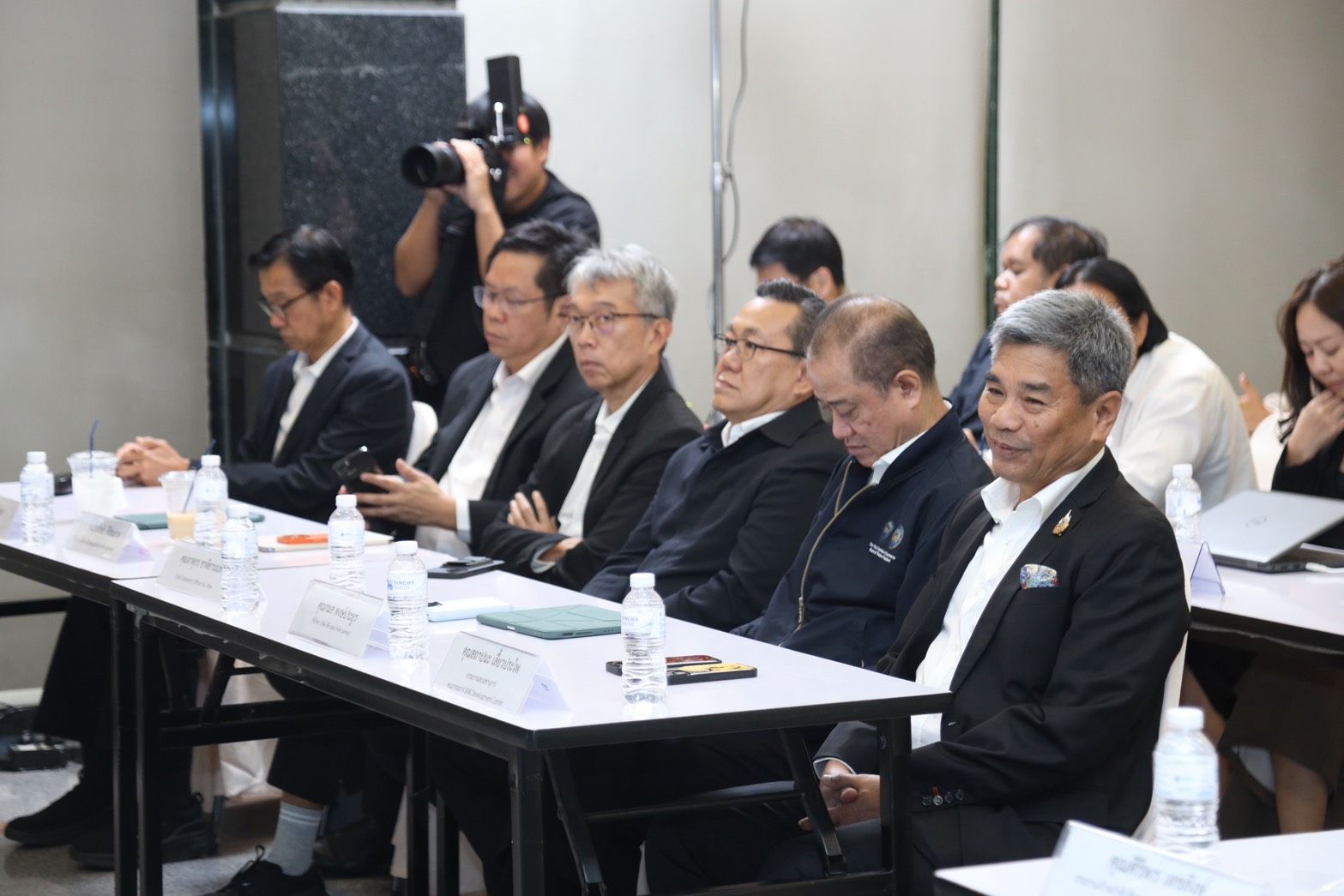 Group of Asian men in business attire attending a meeting, with a photographer in background.
