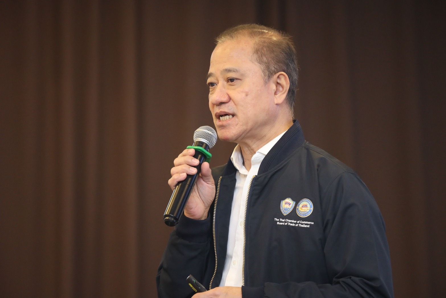 Asian man speaking into a microphone, wearing a dark jacket with a white shirt.
