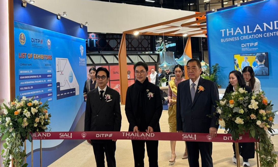 Three men in suits prepare for a ribbon-cutting ceremony at an exhibition booth.