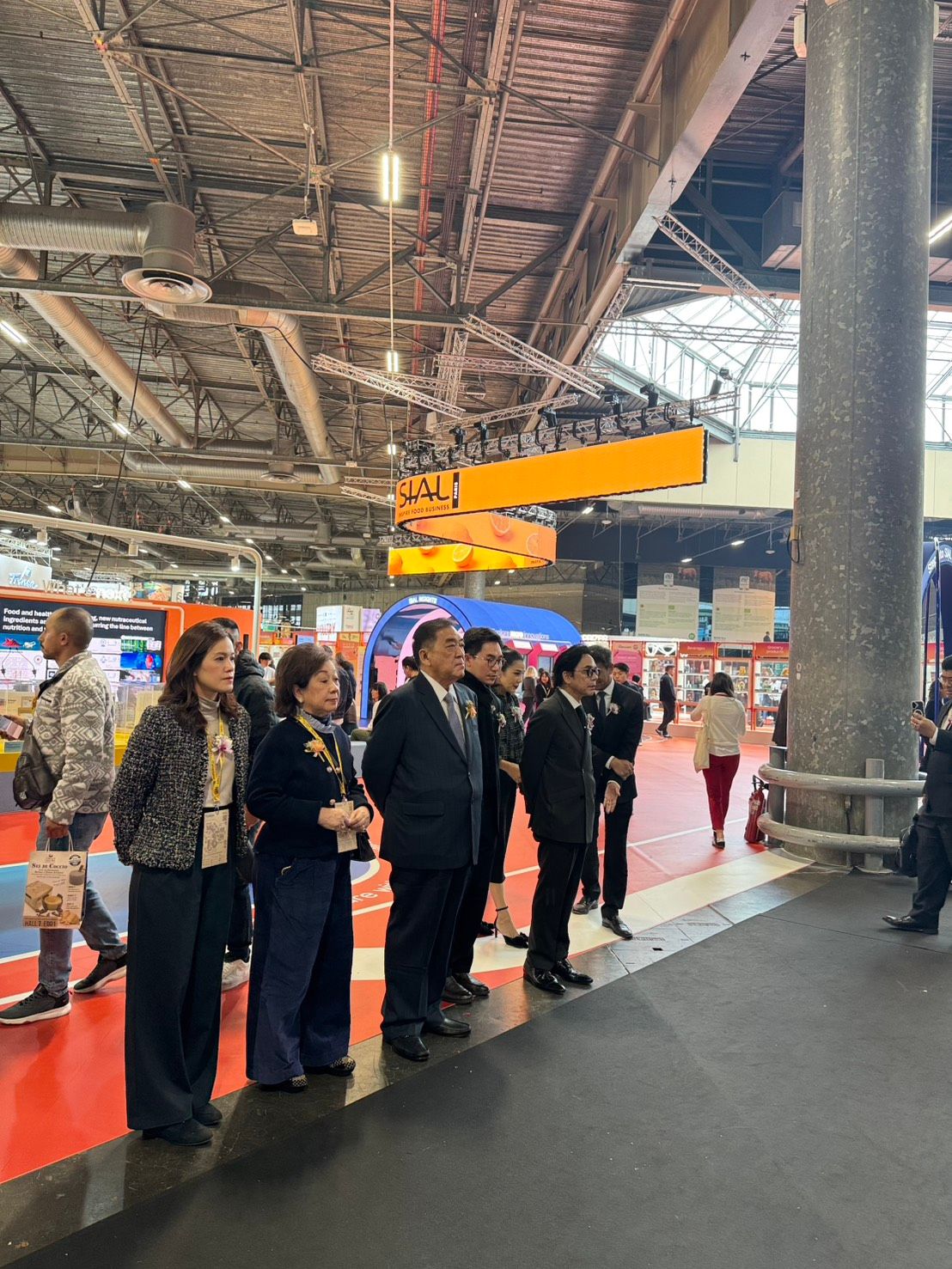 A group of professionals stands attentively in a large, bustling exhibition hall.