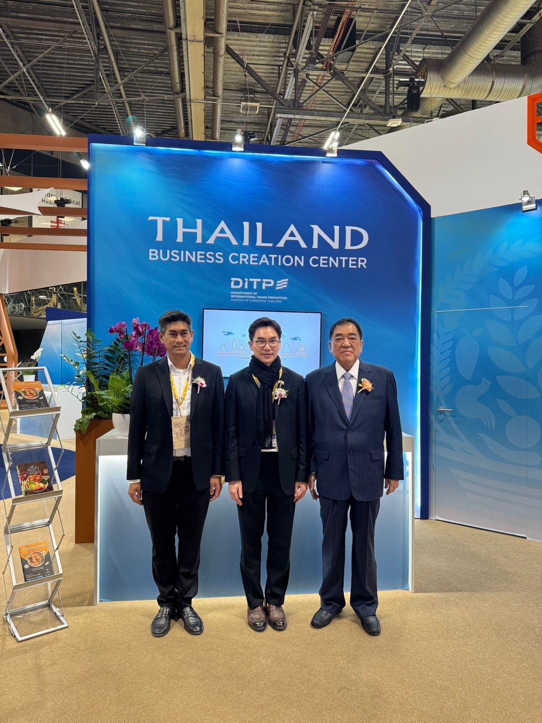 Three men in suits stand before the Thailand Business Innovation Center booth.