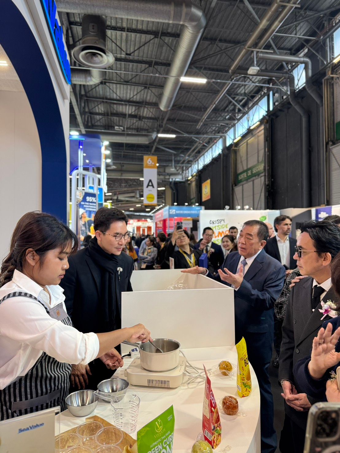 A person in an apron prepares a sample at a busy exhibition booth.