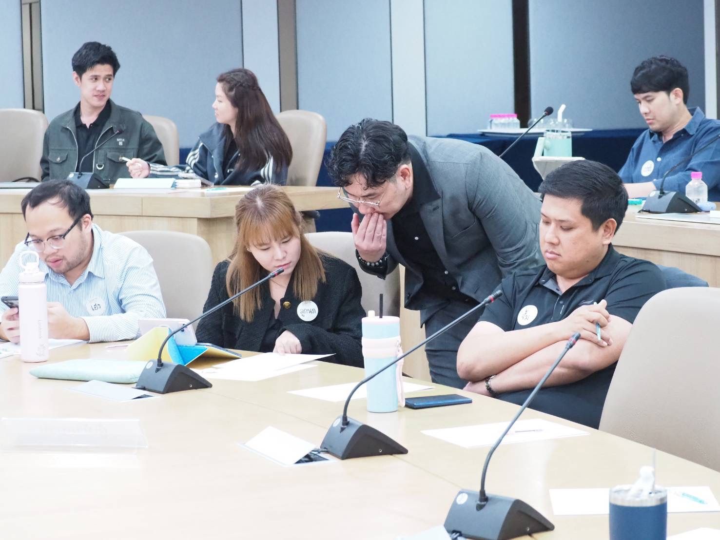 Professionals gather around a long table with microphones during a formal meeting.