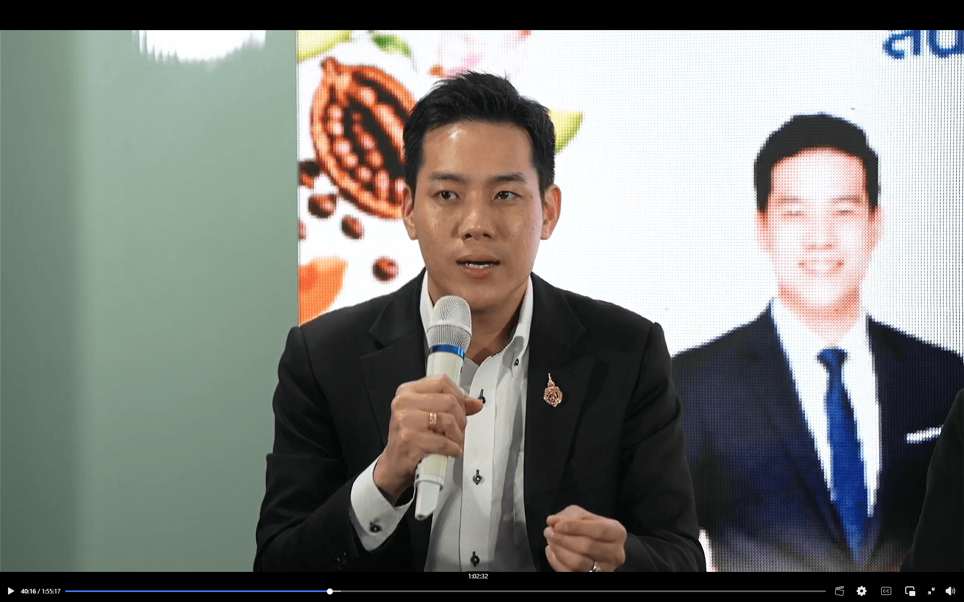 Man in a suit speaks into a microphone at a business presentation.