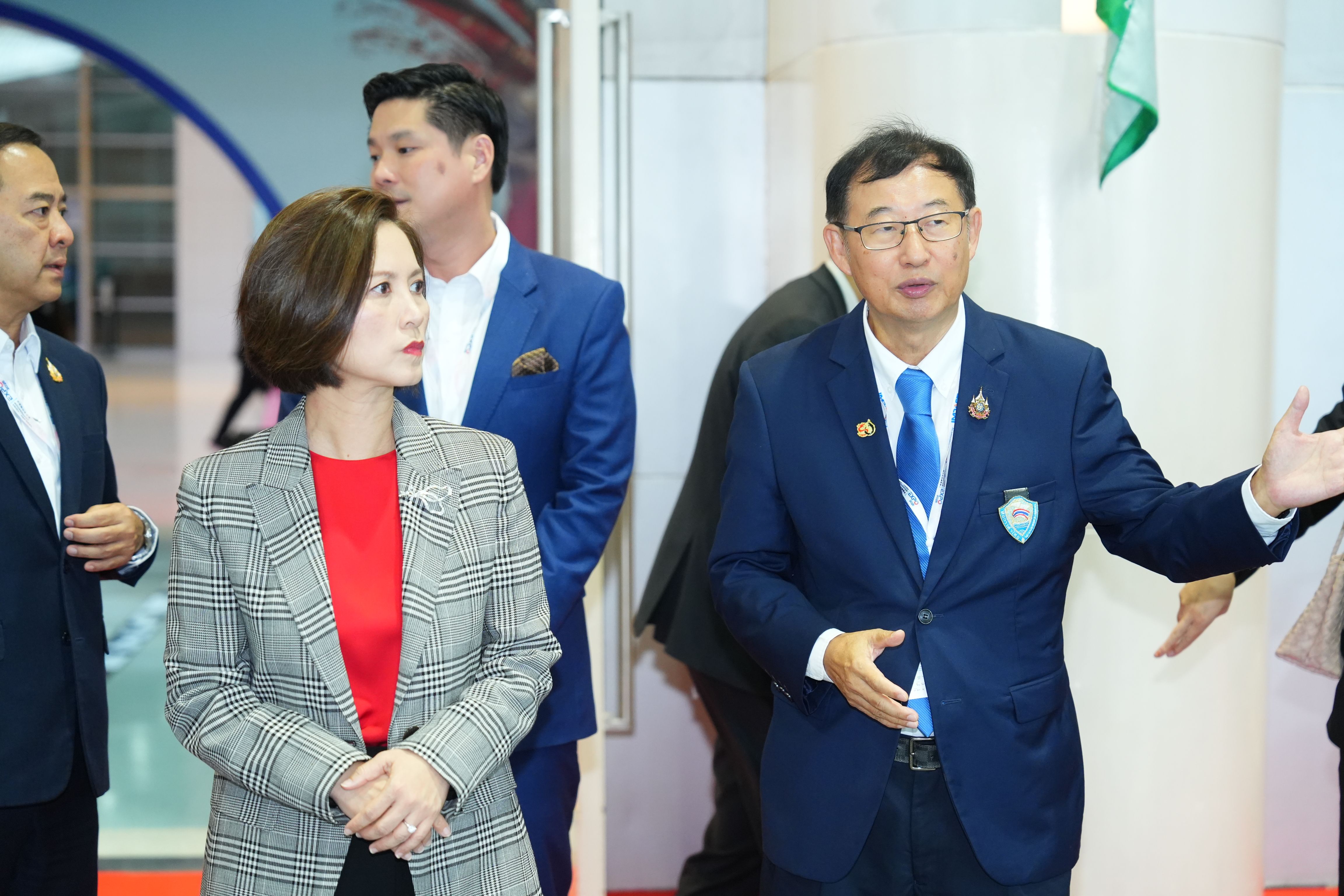 Man in blue suit gestures while woman in plaid blazer observes during a professional event.