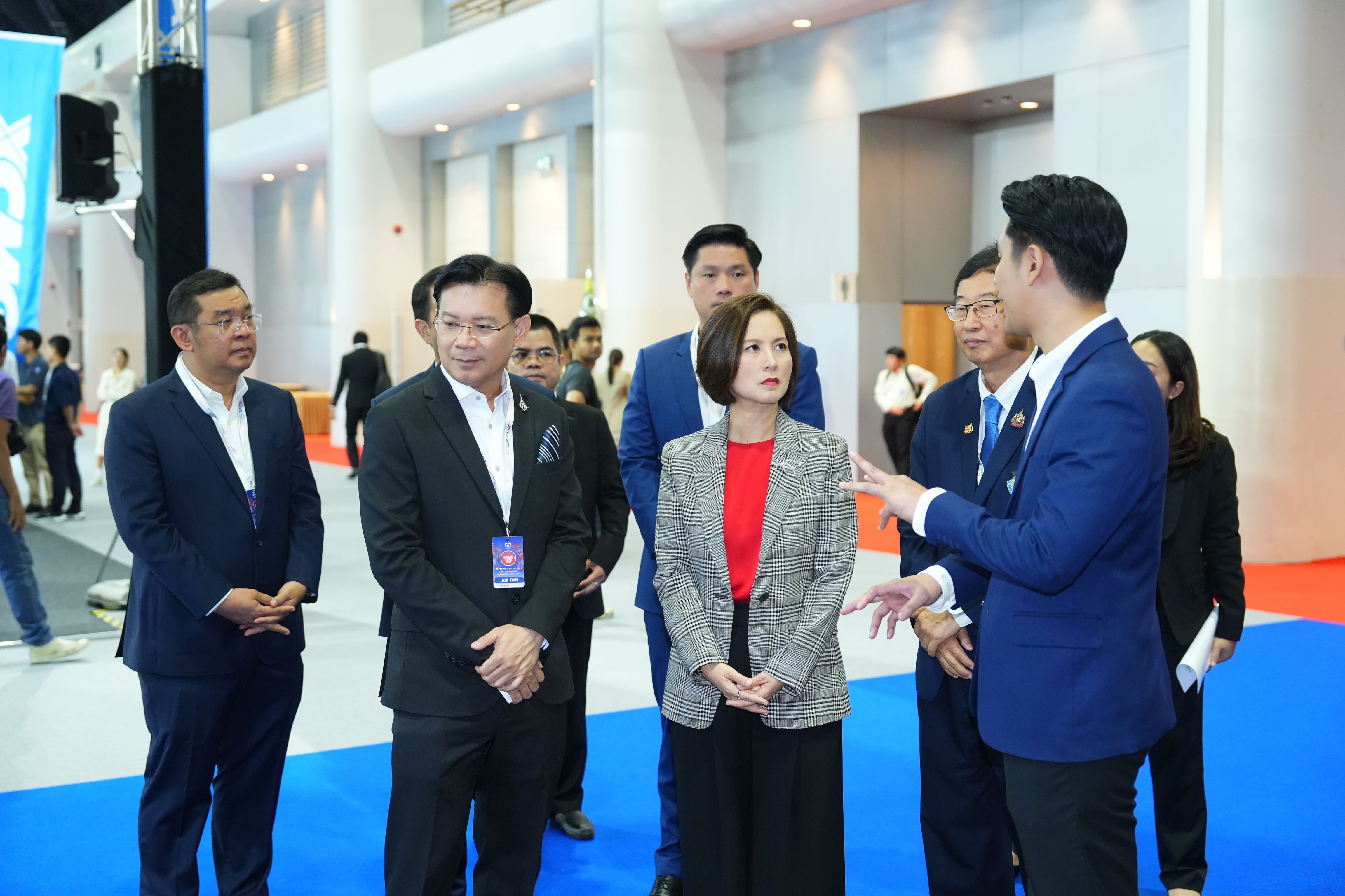 A group of professionals, including men in suits and a woman, converse in a large exhibition hall.
