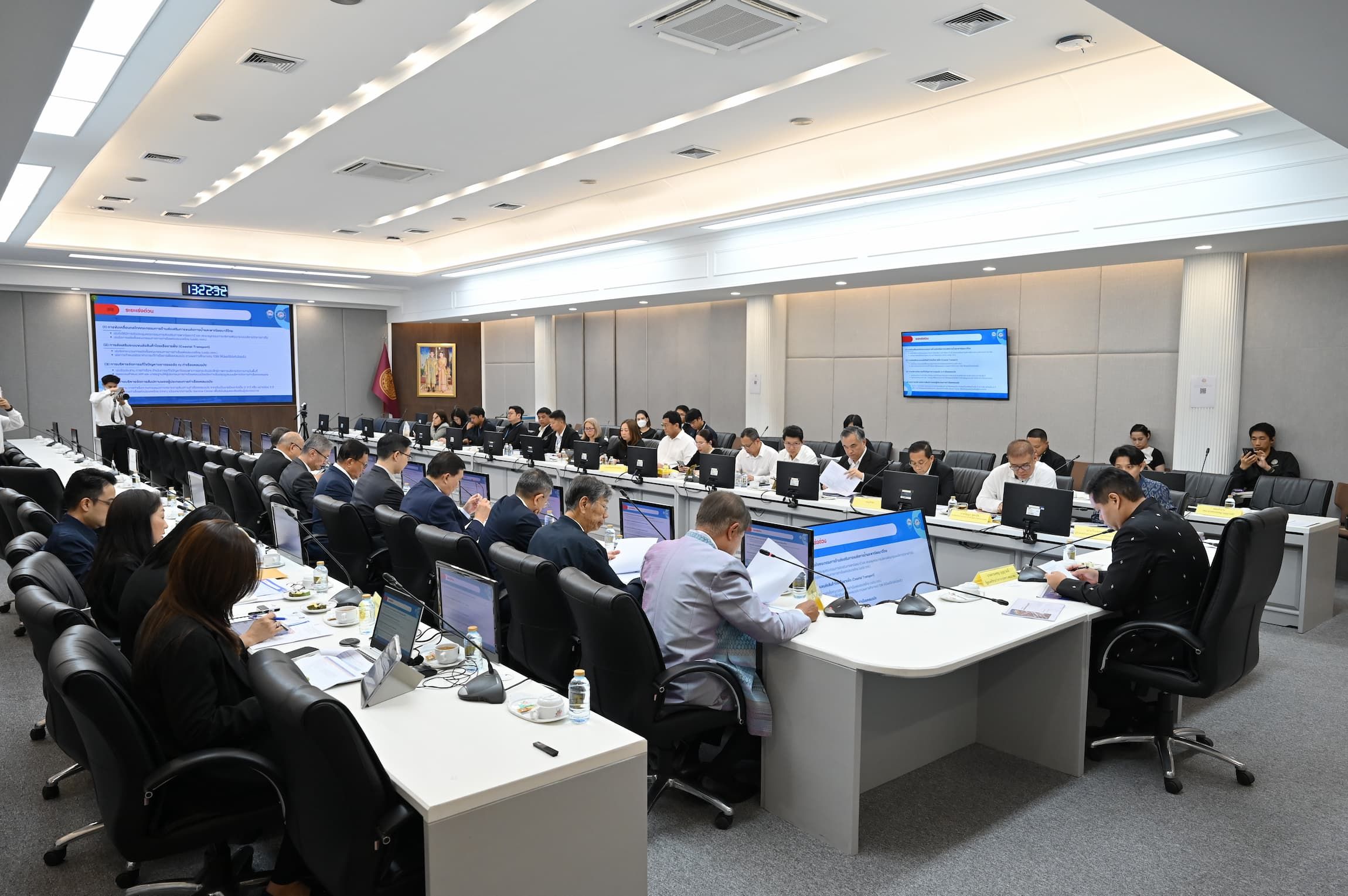 Attendees participate in a formal meeting within a large, modern conference room with multiple screens.