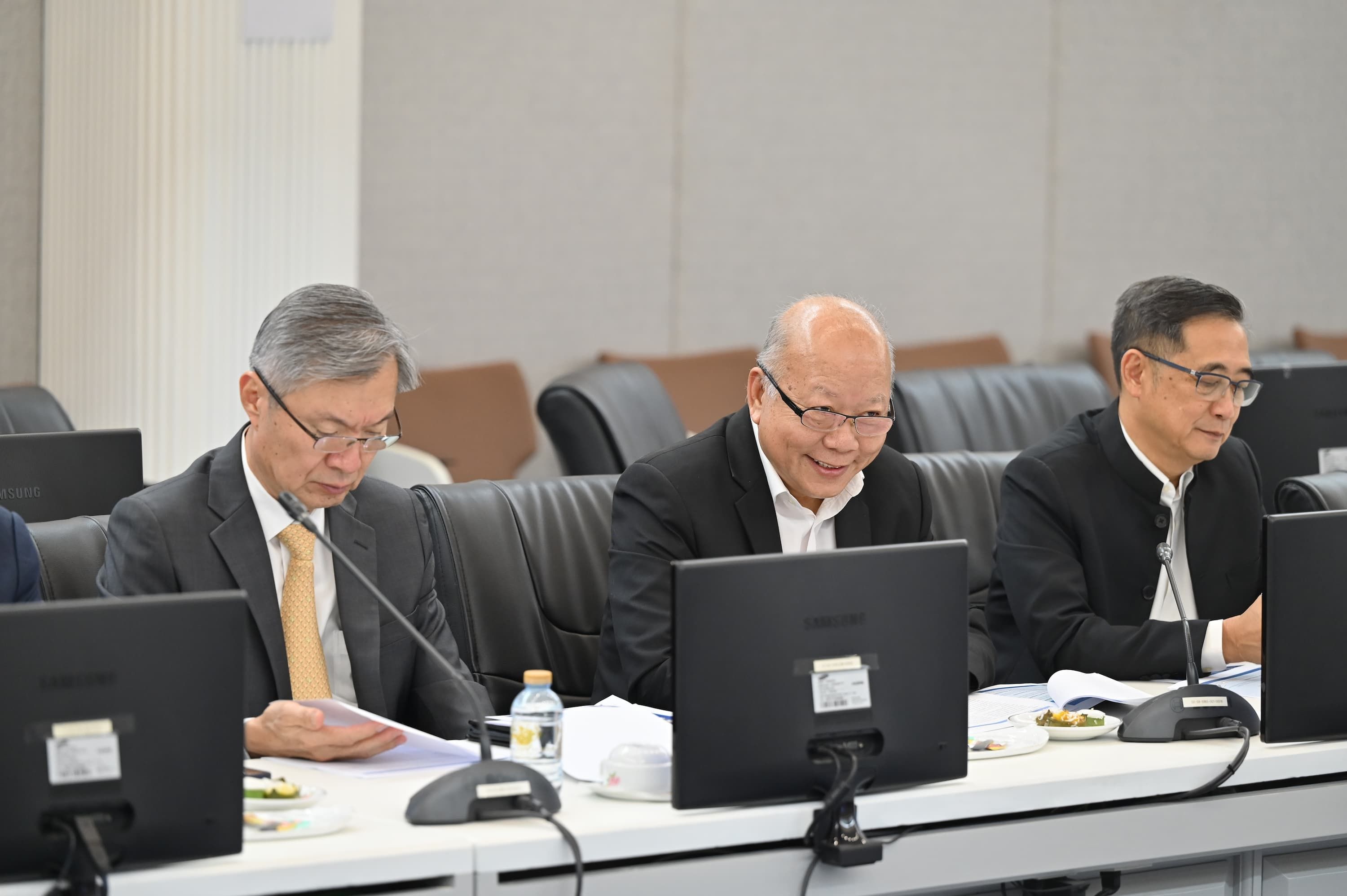 Three men in business attire work on laptops at a conference table.
