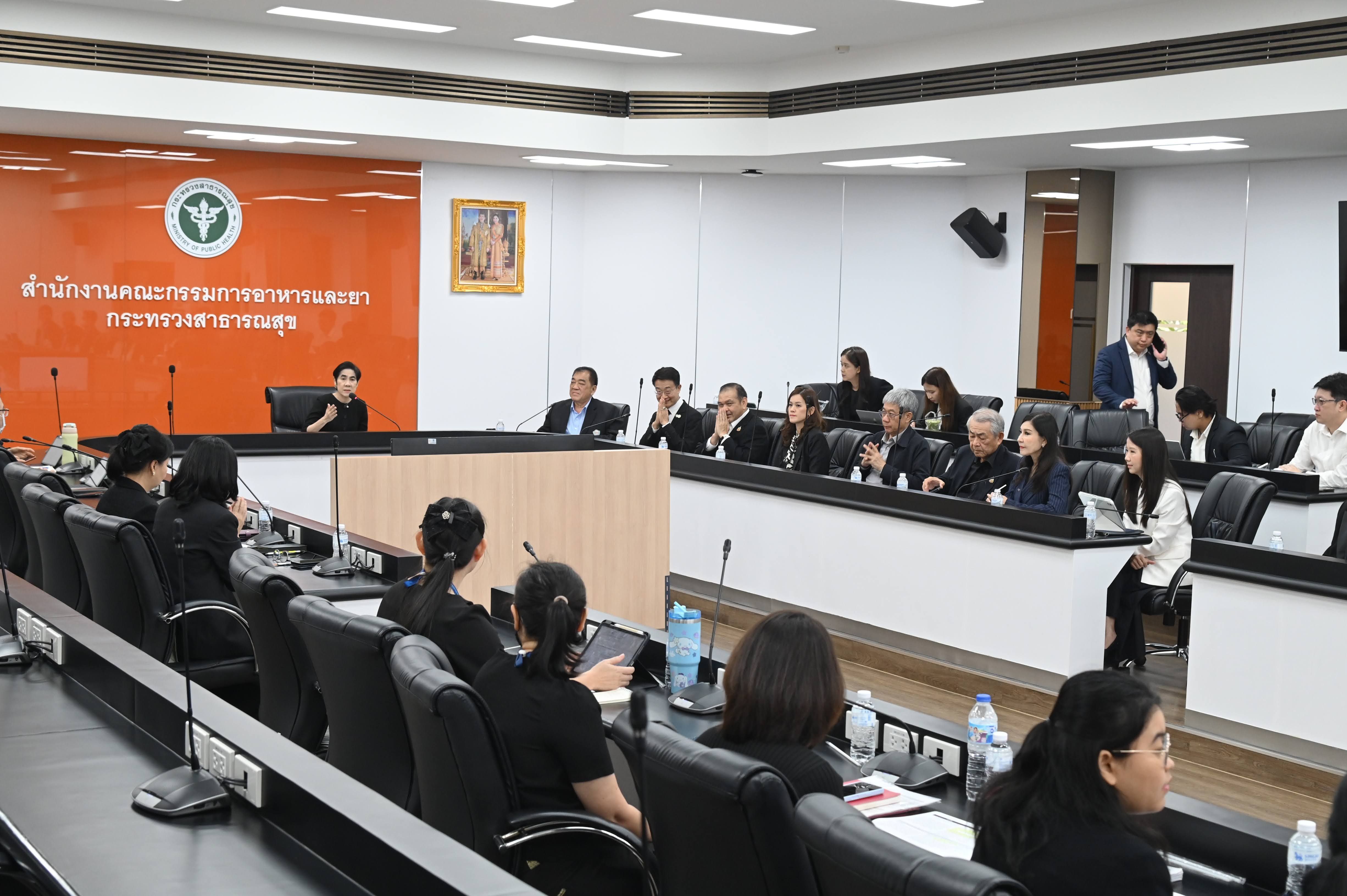 Professionals attend a formal meeting in a conference room with a speaker at the front.