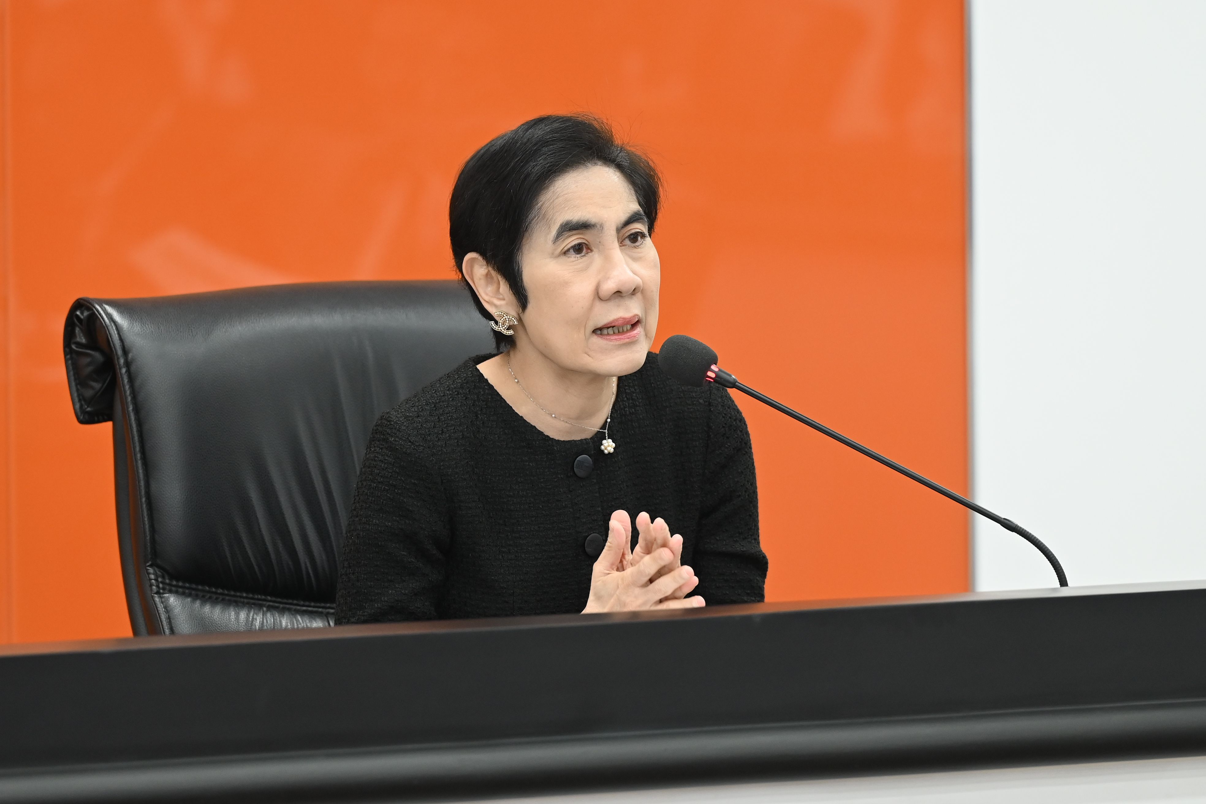 A woman with dark hair speaks into a microphone at a professional event.