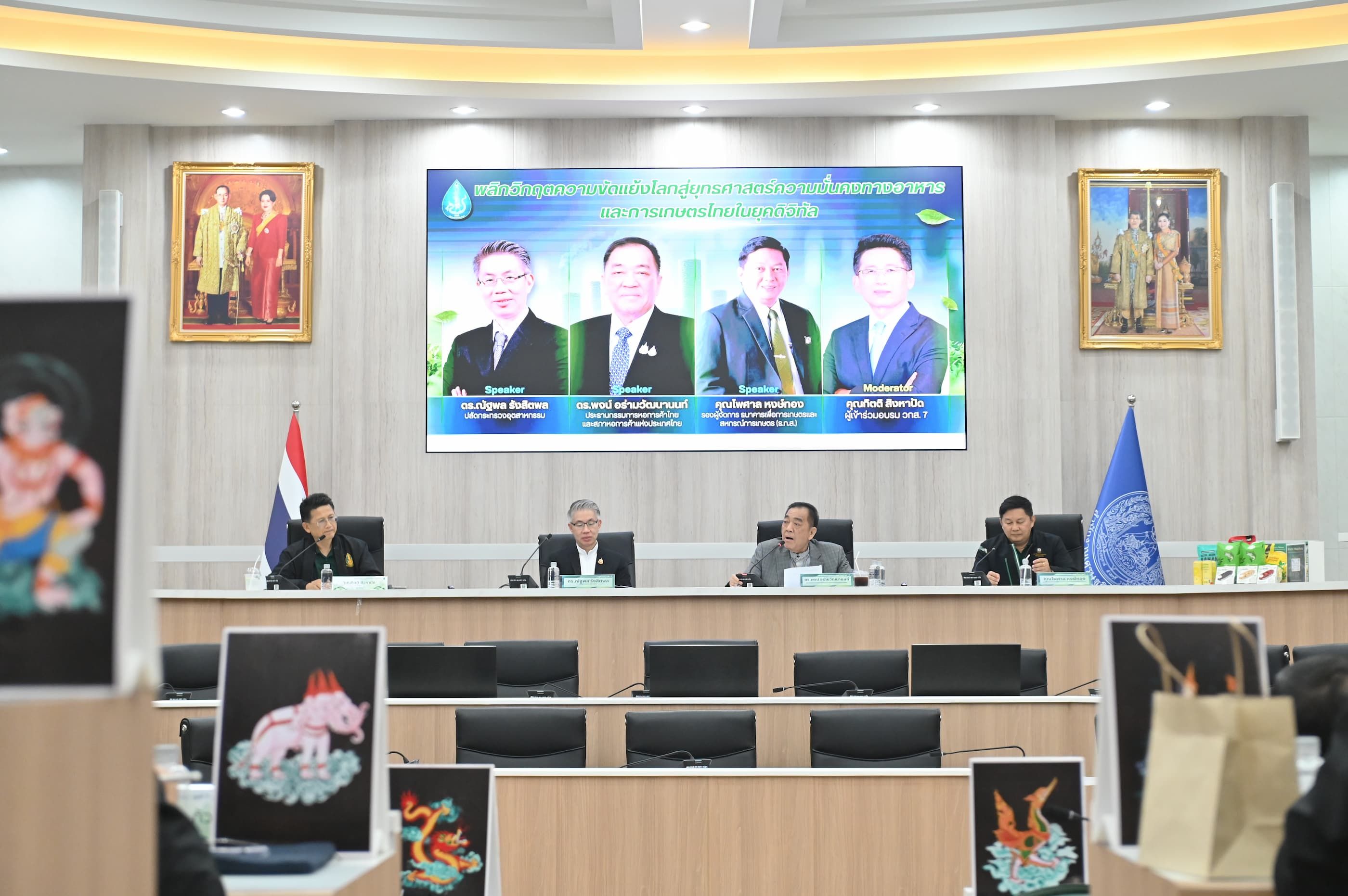 Formal meeting with officials at a long table and a large screen displaying four men.