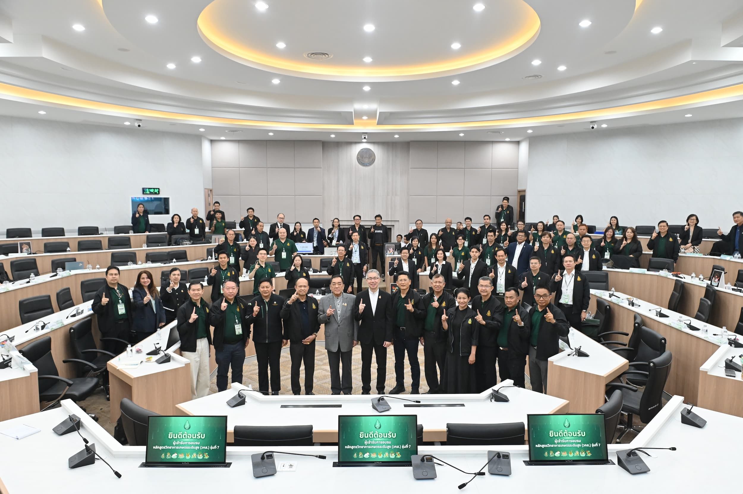 A large group of formally dressed people stand in a modern conference room posing for a photo.