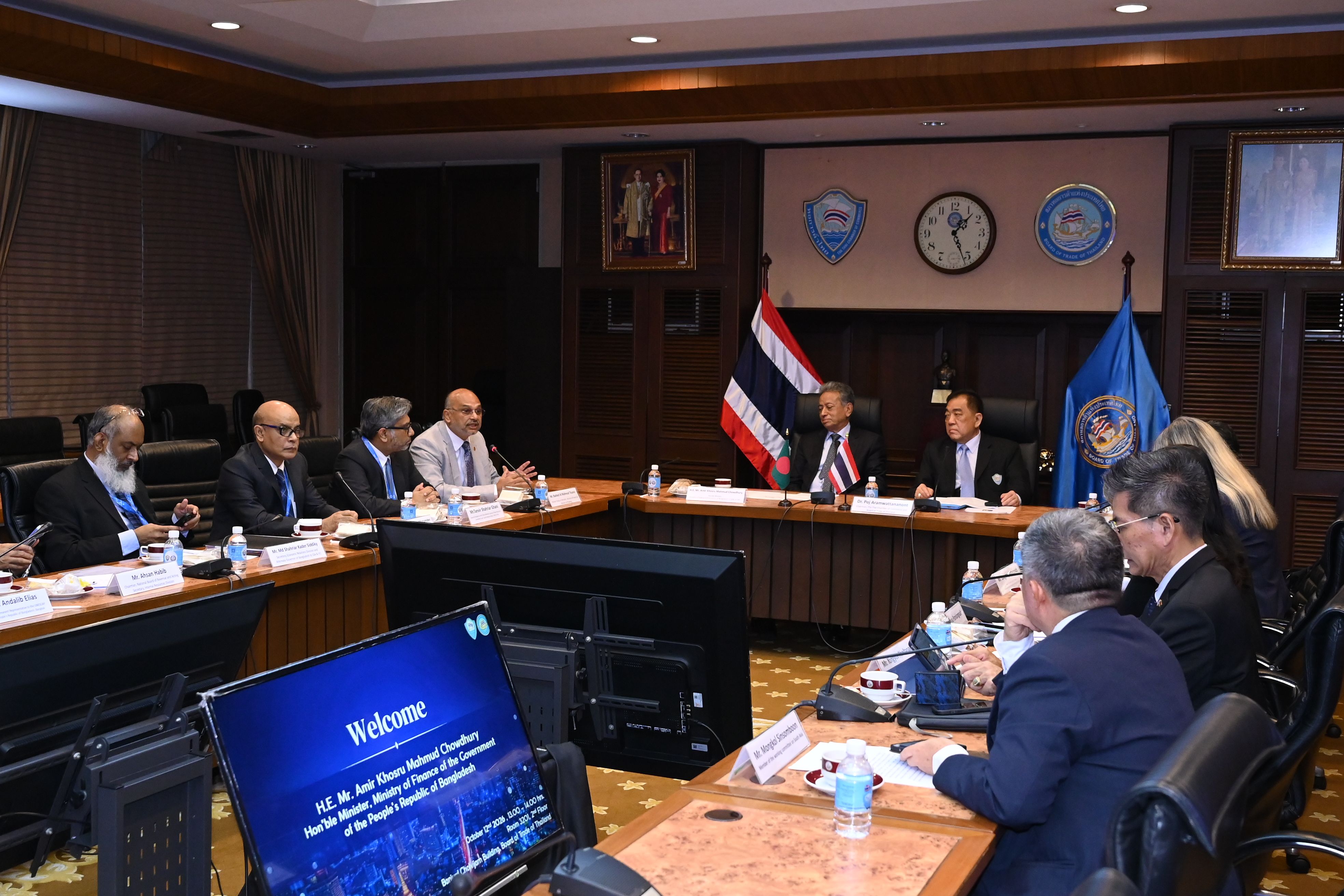 People attending a formal international meeting in a conference room with flags.