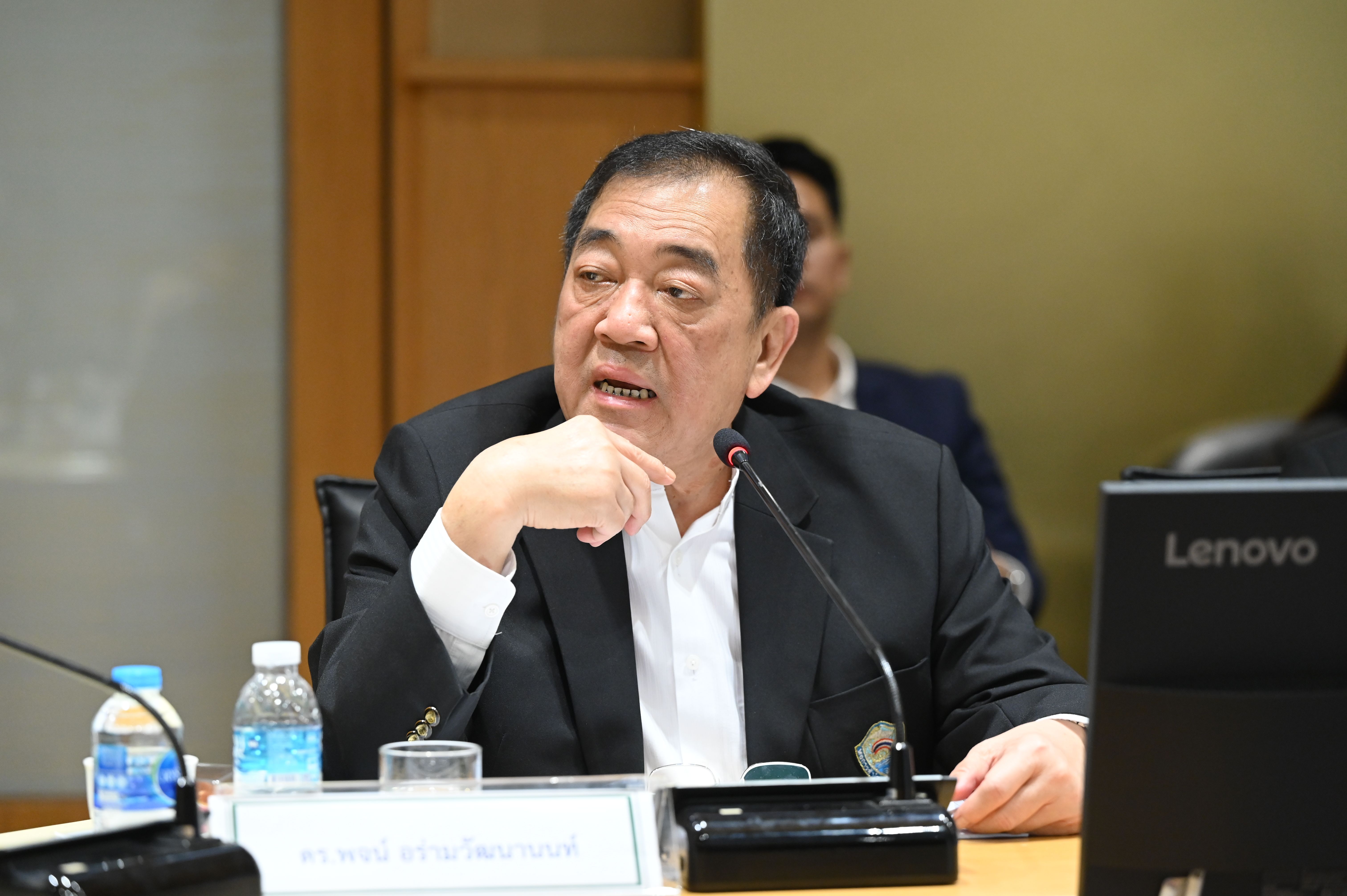 Man in a black suit speaking at a meeting table with a Lenovo laptop.