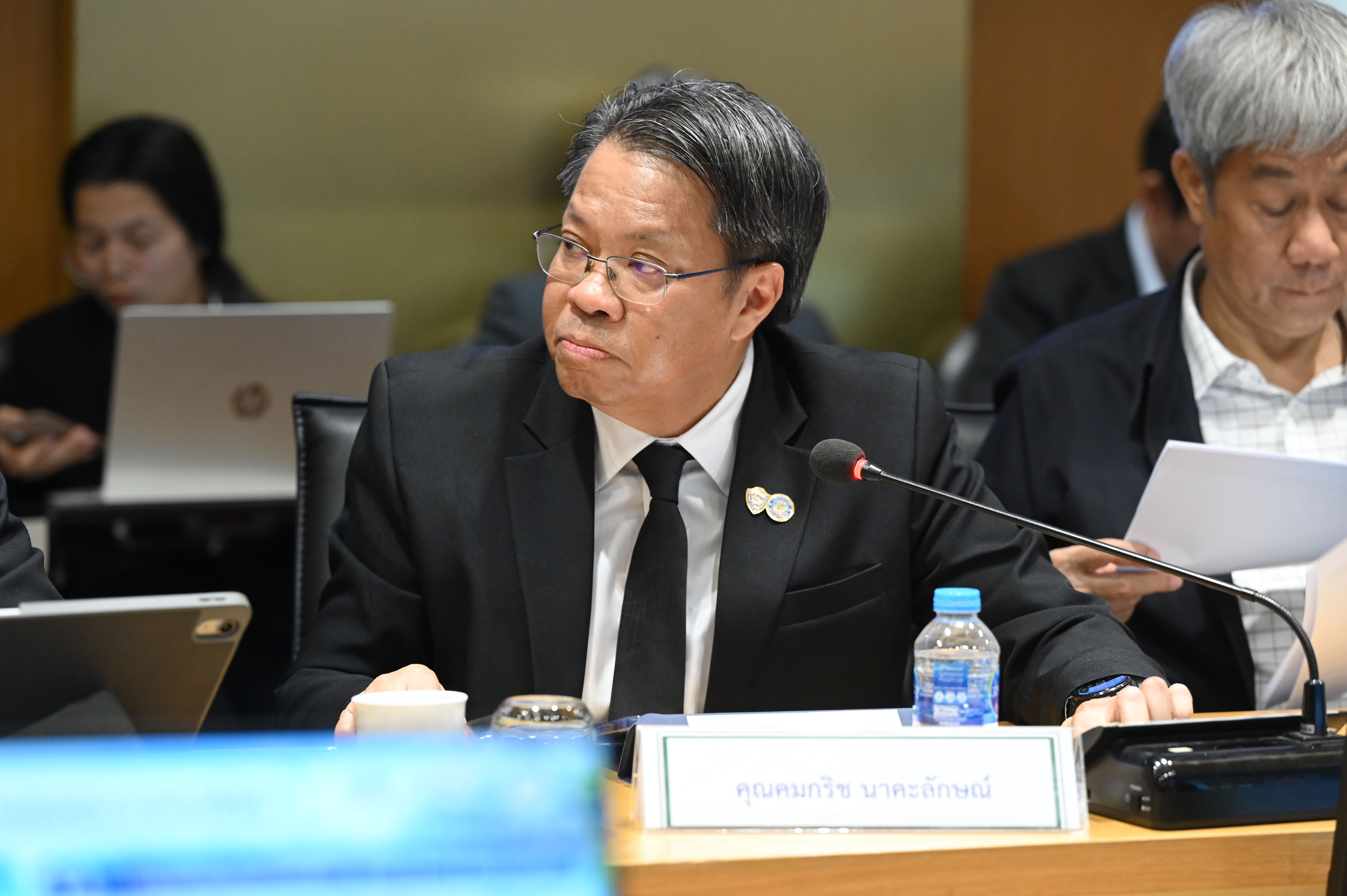 Man in suit and glasses at a conference table, looking intently to his left.