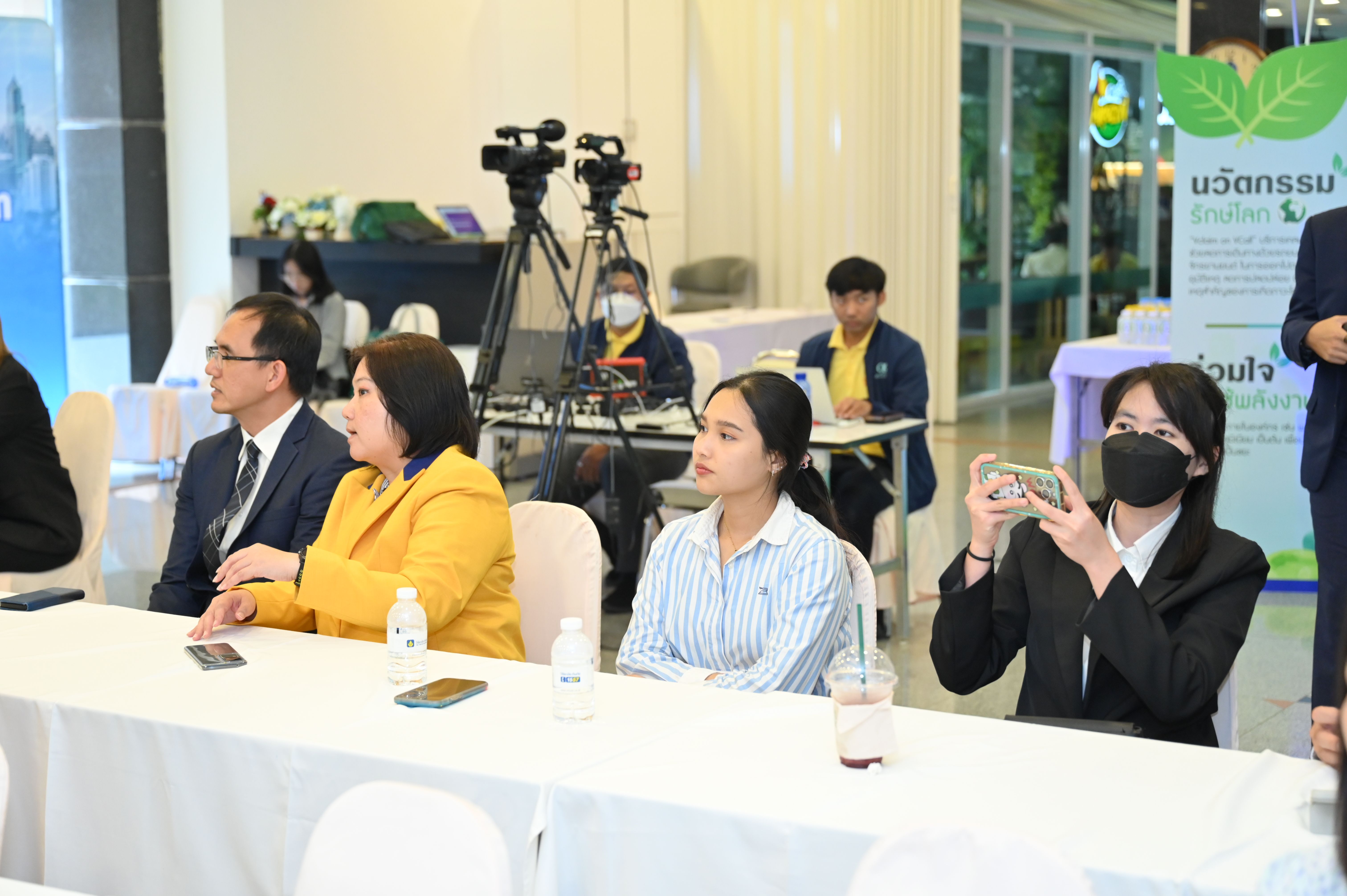 Attendees at a conference or presentation, with one person recording on a phone.