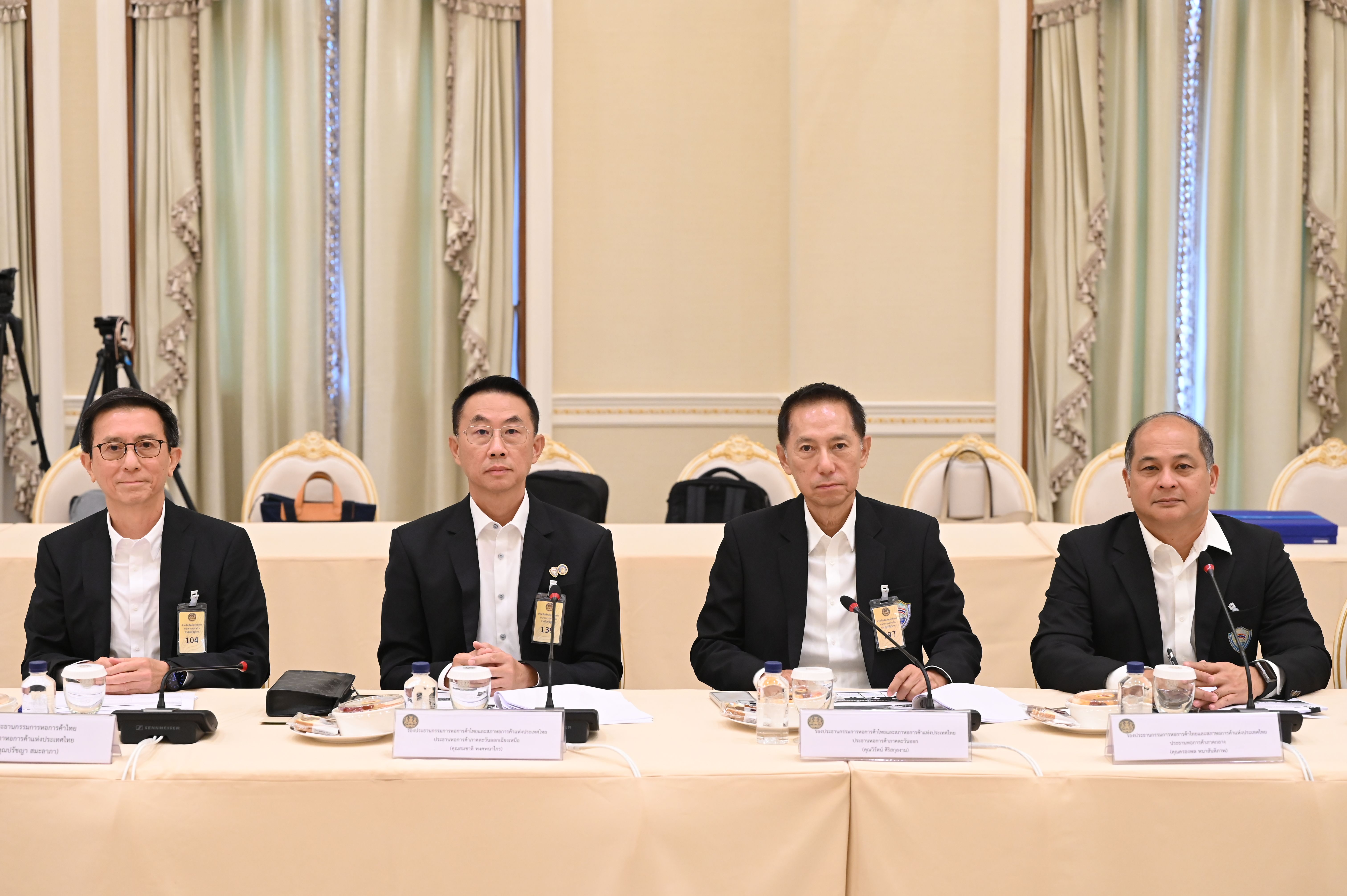 Four men in black suits sit at a long table during a formal meeting.
