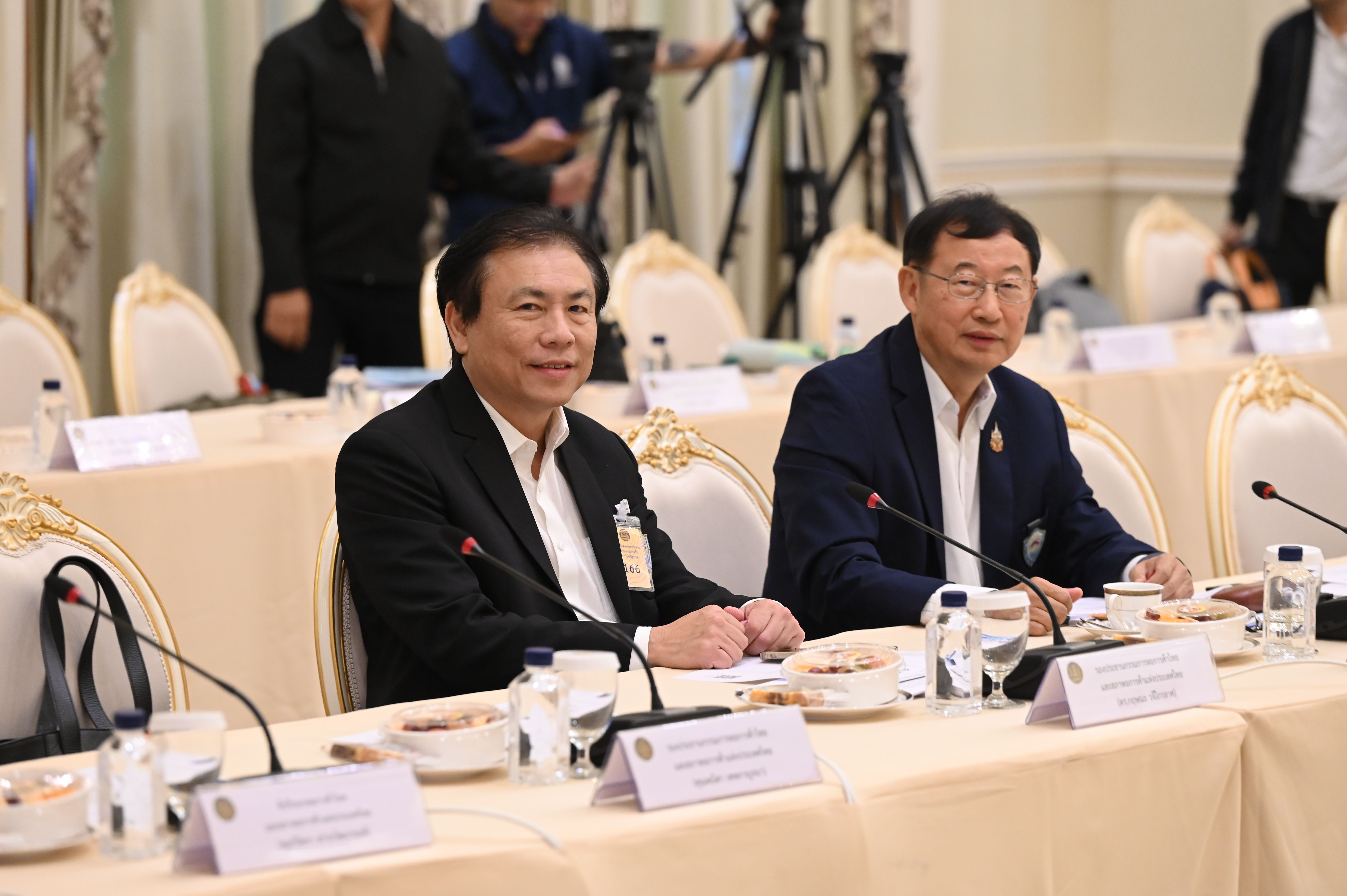 Two Asian men in suits sit at a formal conference table, smiling attentively.