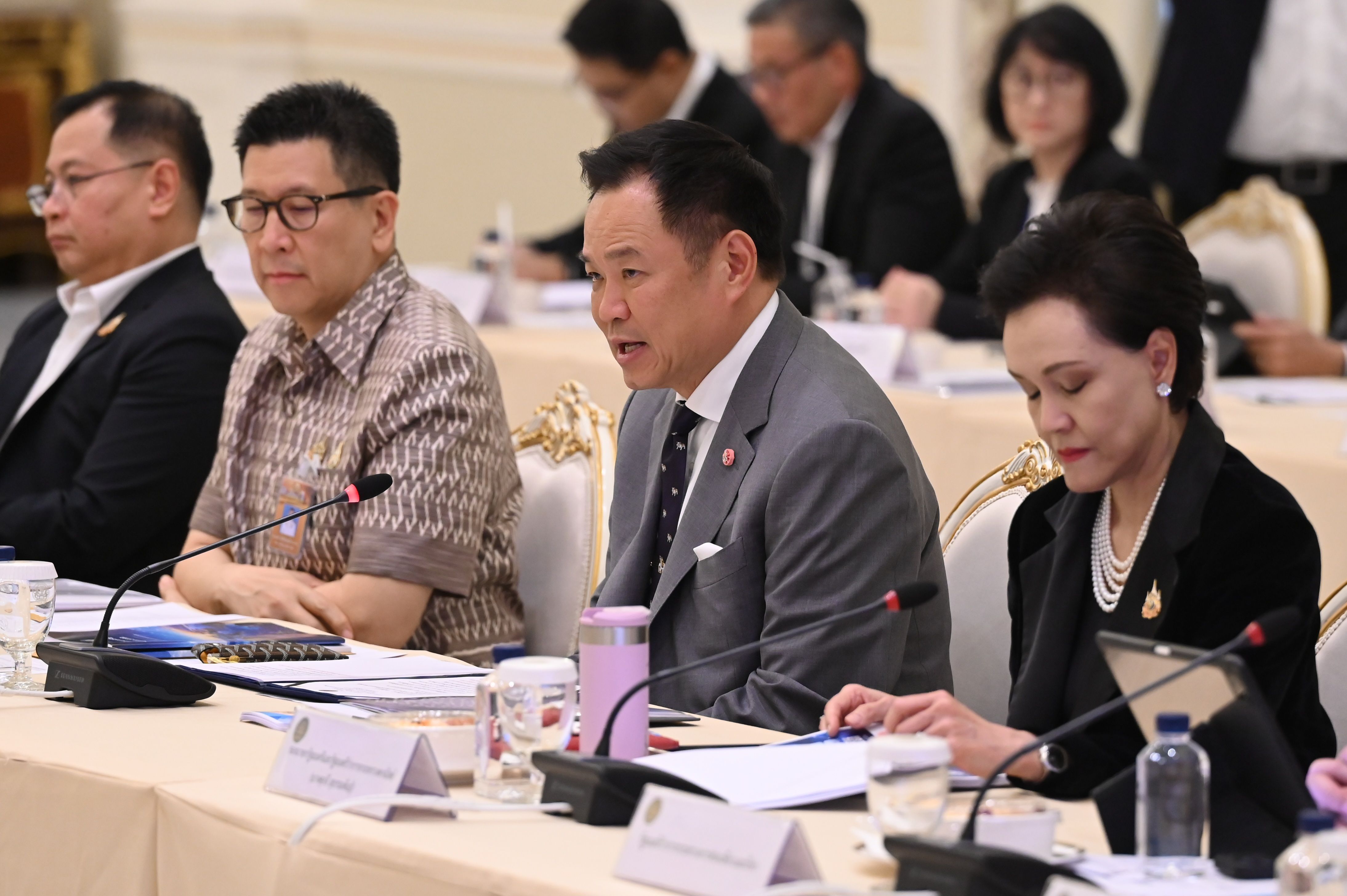 Asian officials in business attire attend a formal meeting, with one man speaking.