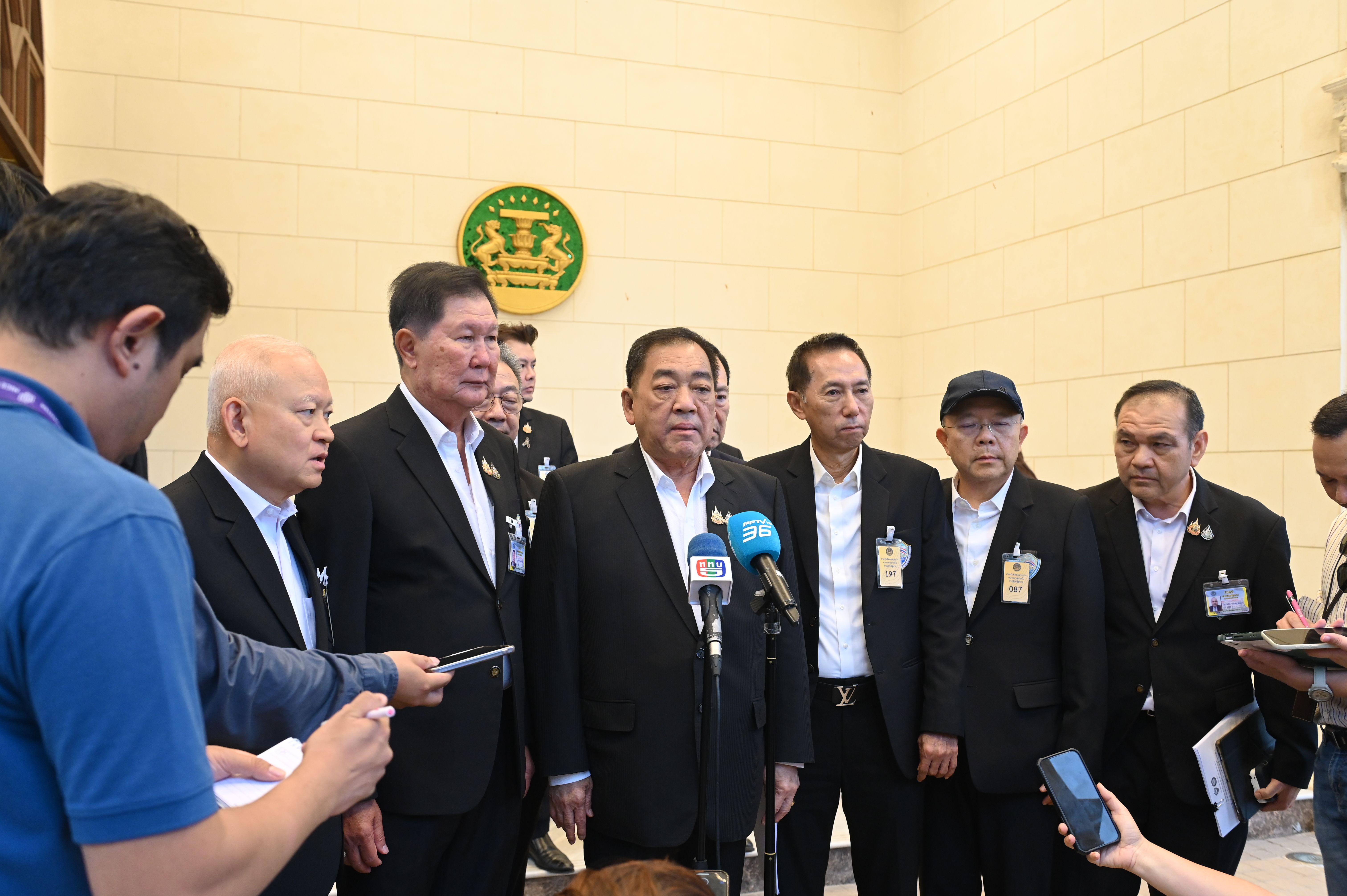 Thai official in a dark suit speaks to media at an indoor press conference.