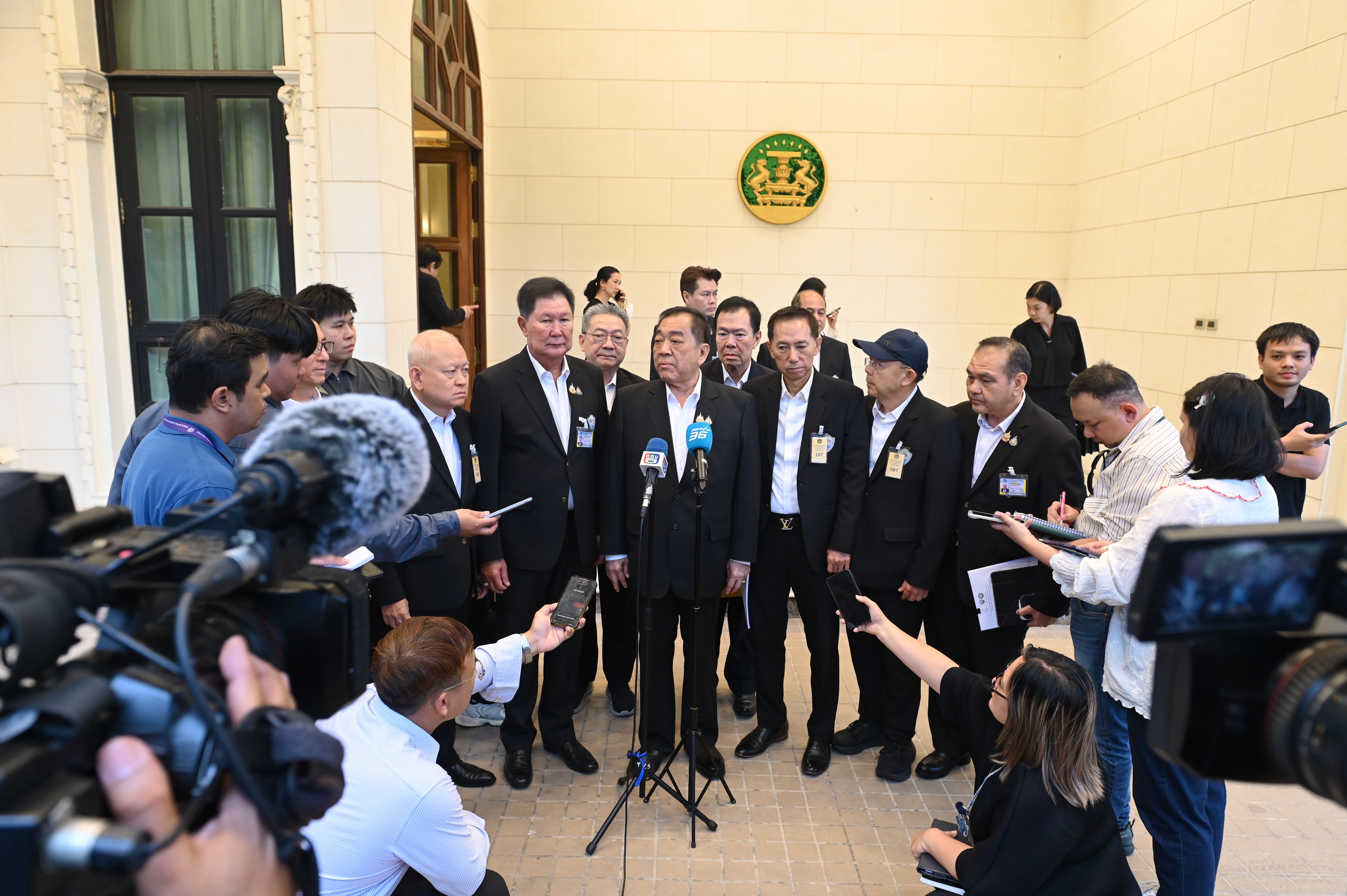 Officials in suits address reporters with microphones at an outdoor press conference.