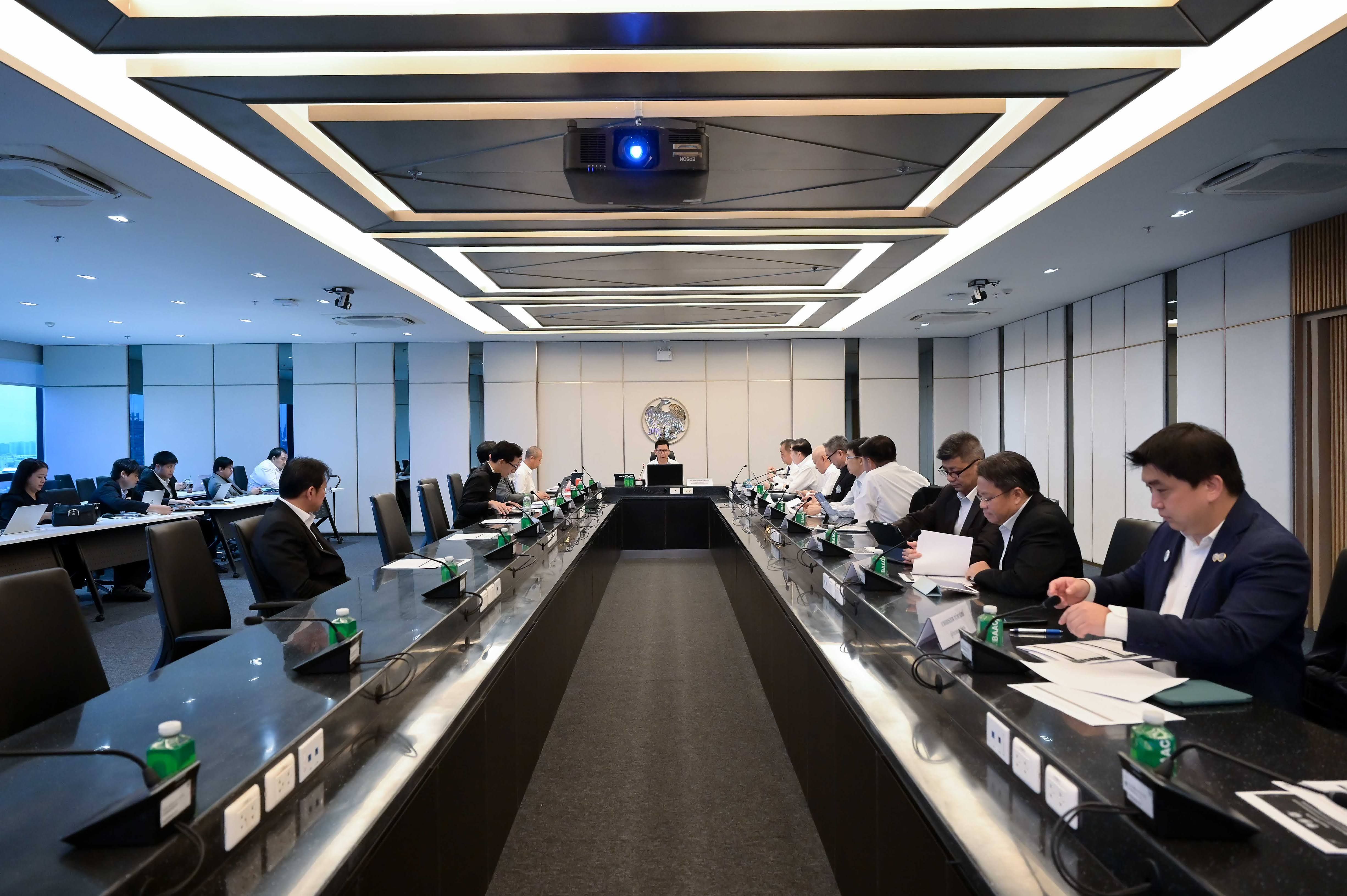 People in business attire seated around a long, dark conference table in a modern room.