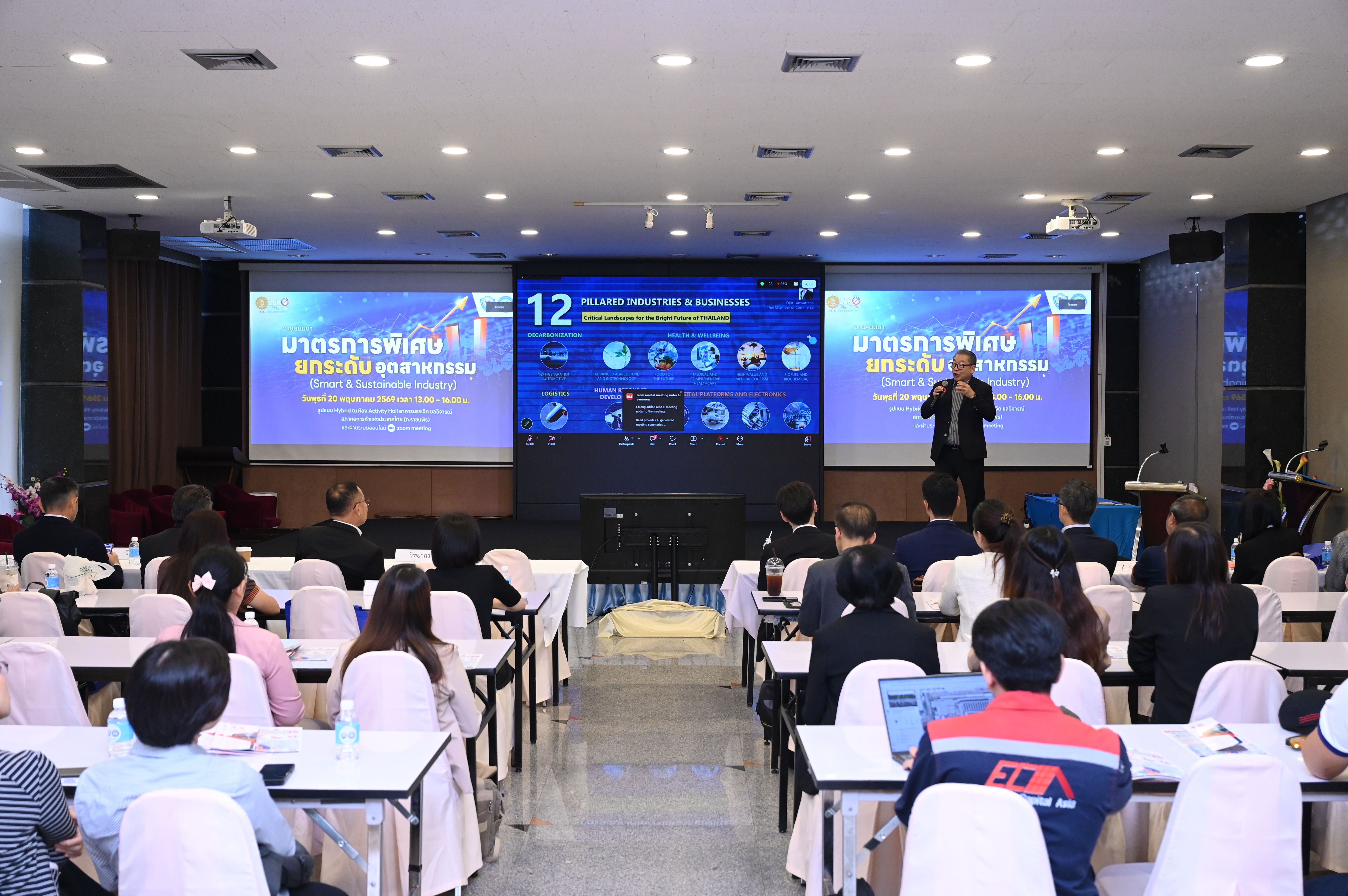 Person presenting on stage to an audience in a conference room with large screens.