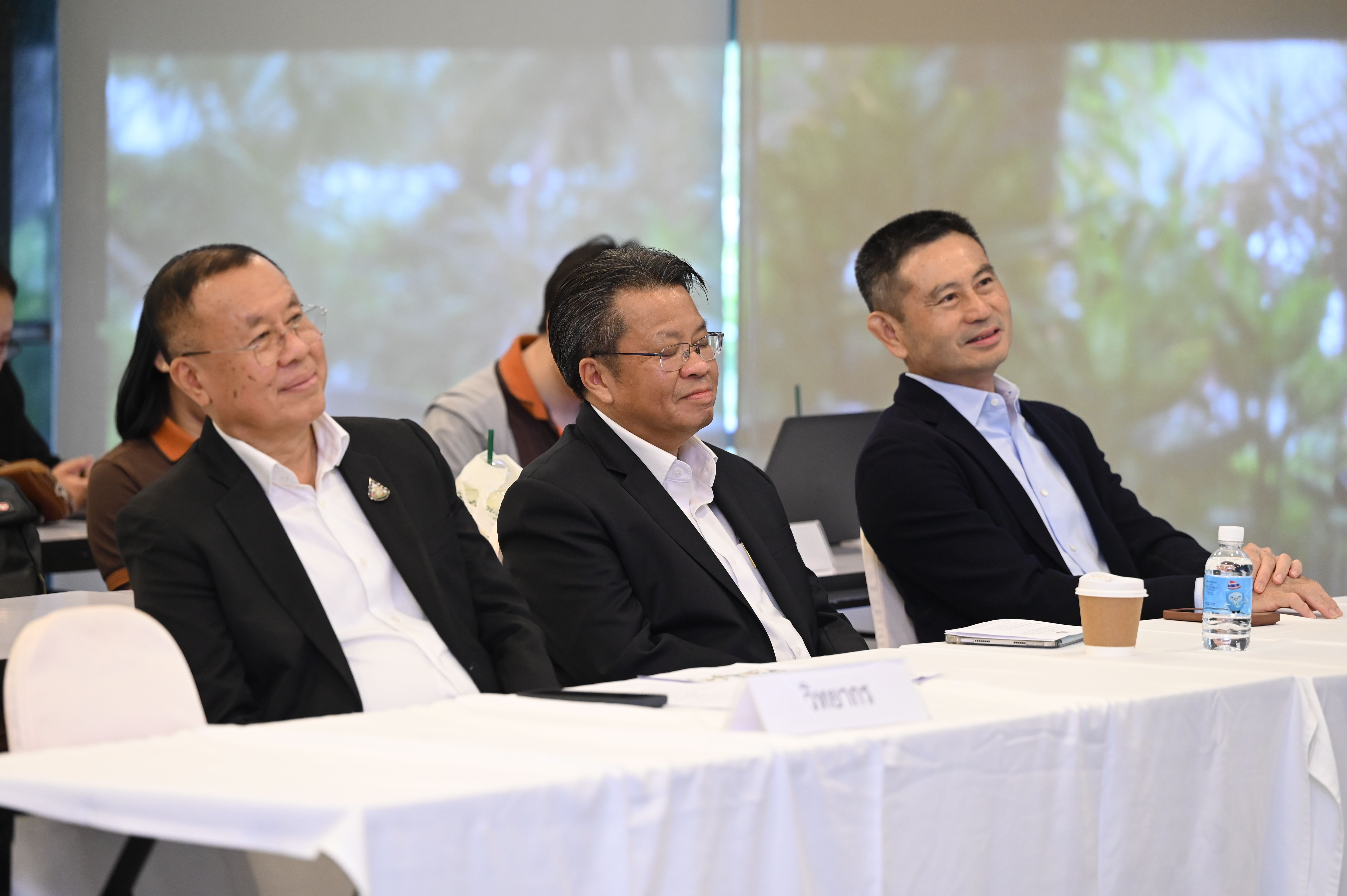 Three attentive men in business attire are seated at a conference table, observing a presentation.
