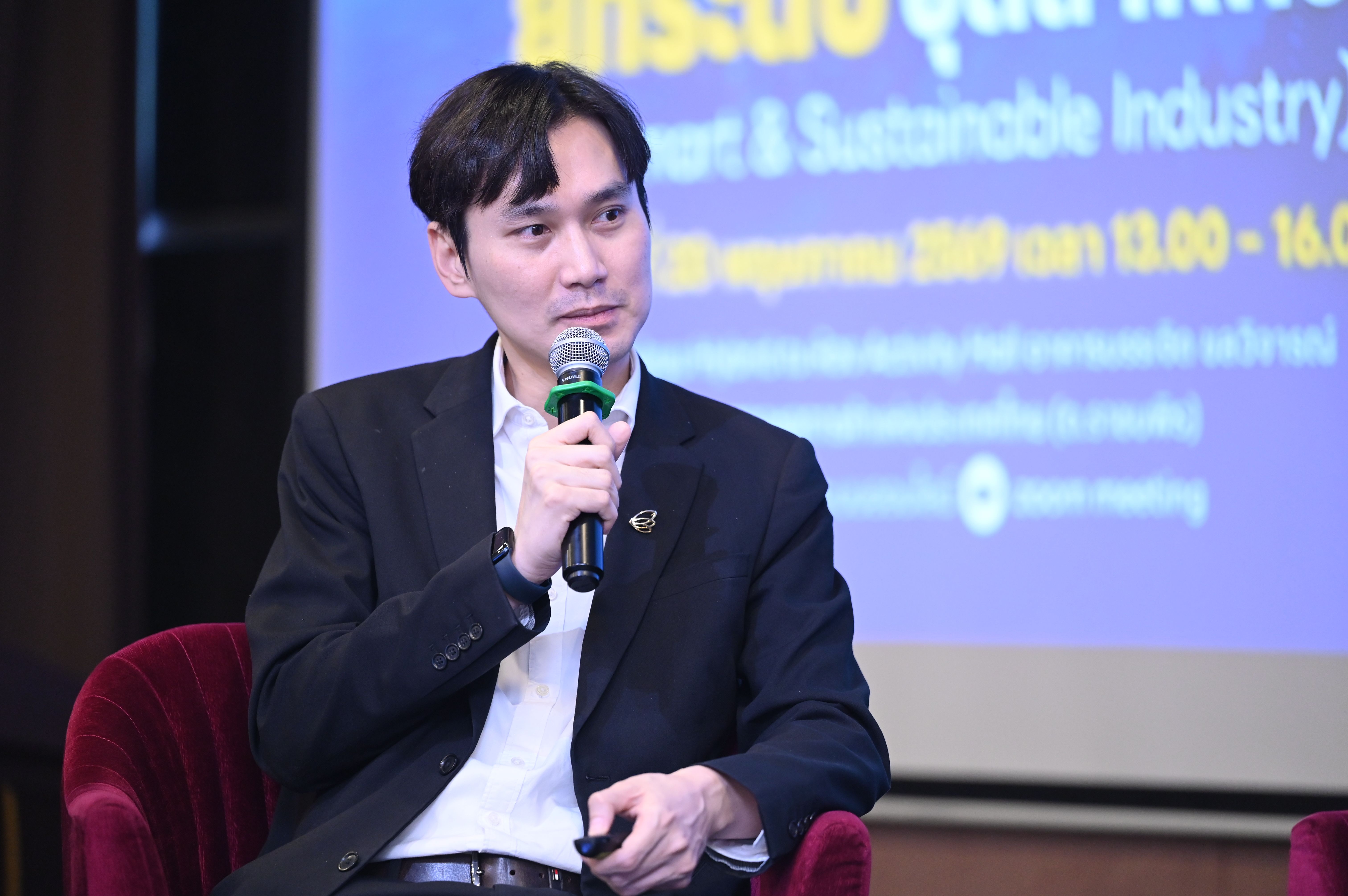 Man in dark suit speaking into a microphone at an industry event.