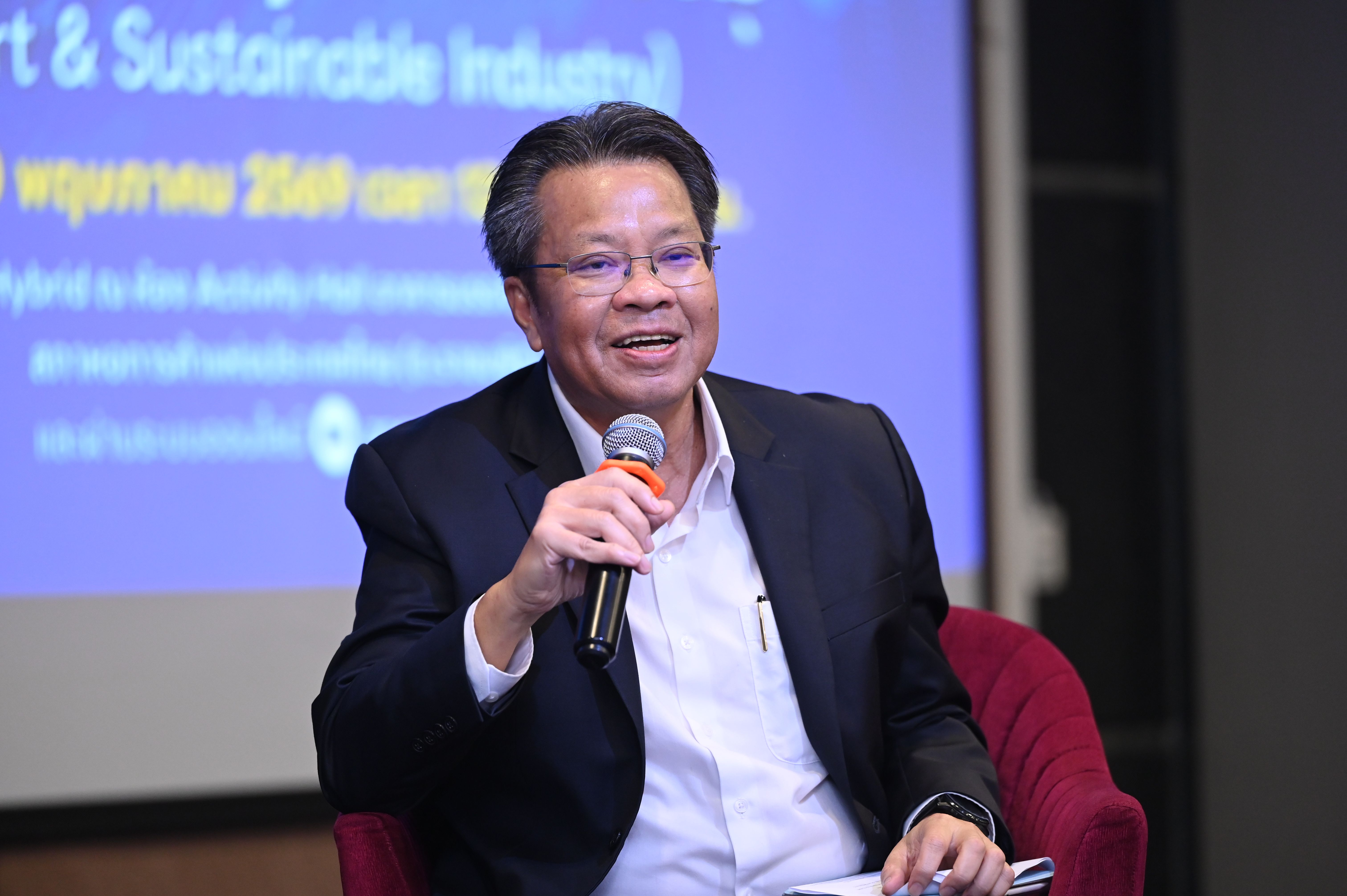 Man in glasses and suit speaking into a microphone at an event.
