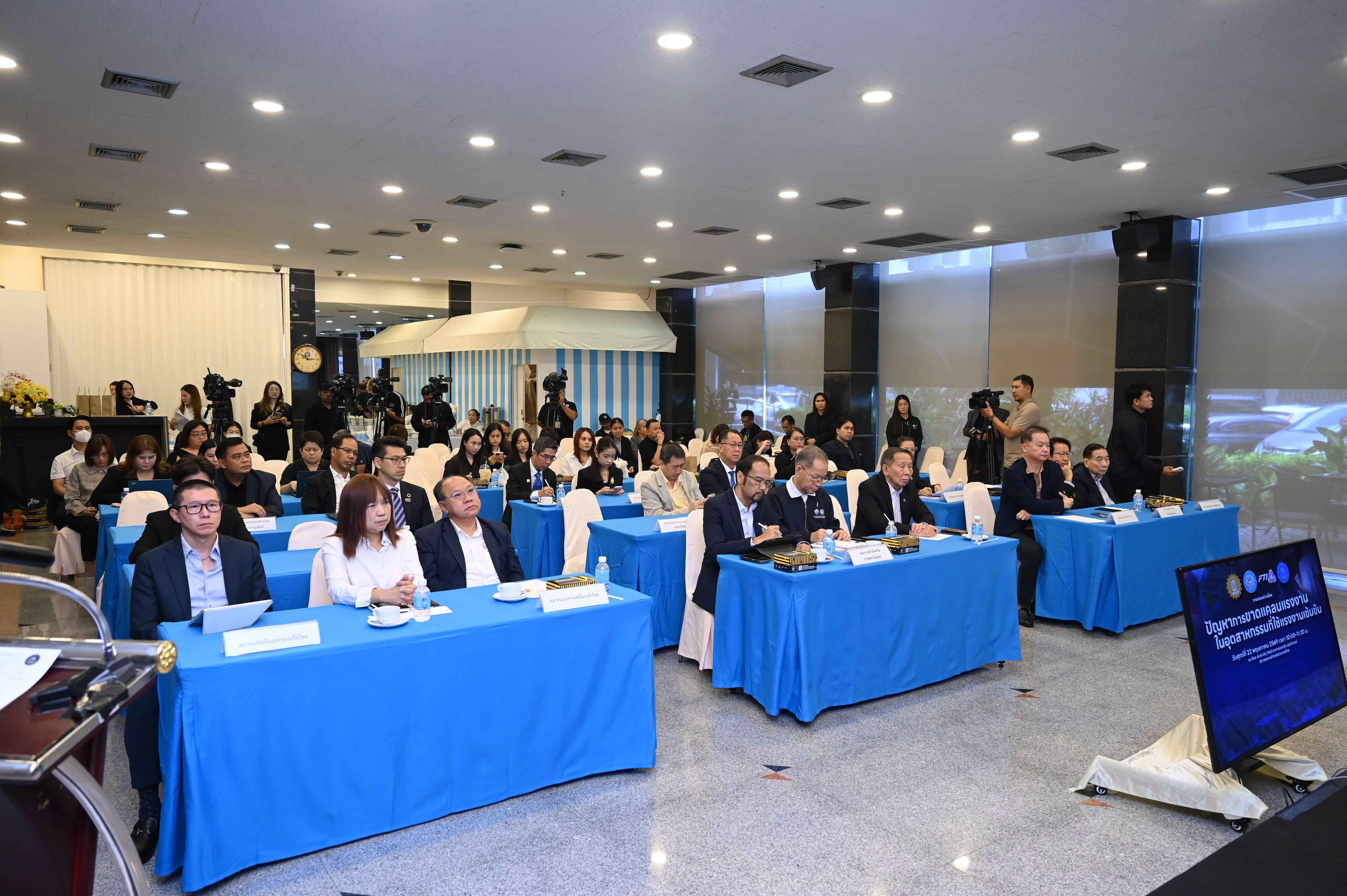 Attendees seated at blue-covered tables listen to a presentation at a professional conference.