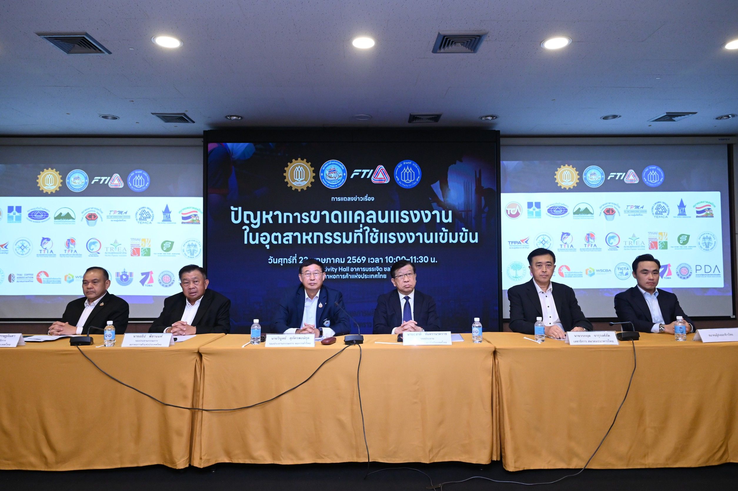 Six men in suits at a conference table with a large screen displaying Thai text.